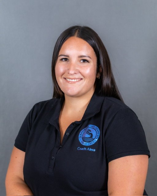 A woman with curly black hair, glasses, and a nose ring smiling and talking to a man with short hair, sitting on a blue couch with a blue pillow, engaging in conversation.