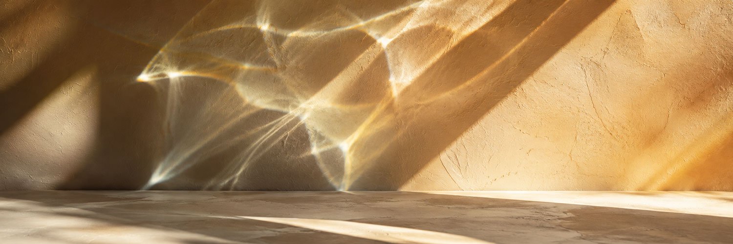 Sunlight reflecting through a glass, creating light patterns on a textured beige wall and a marble floor.
