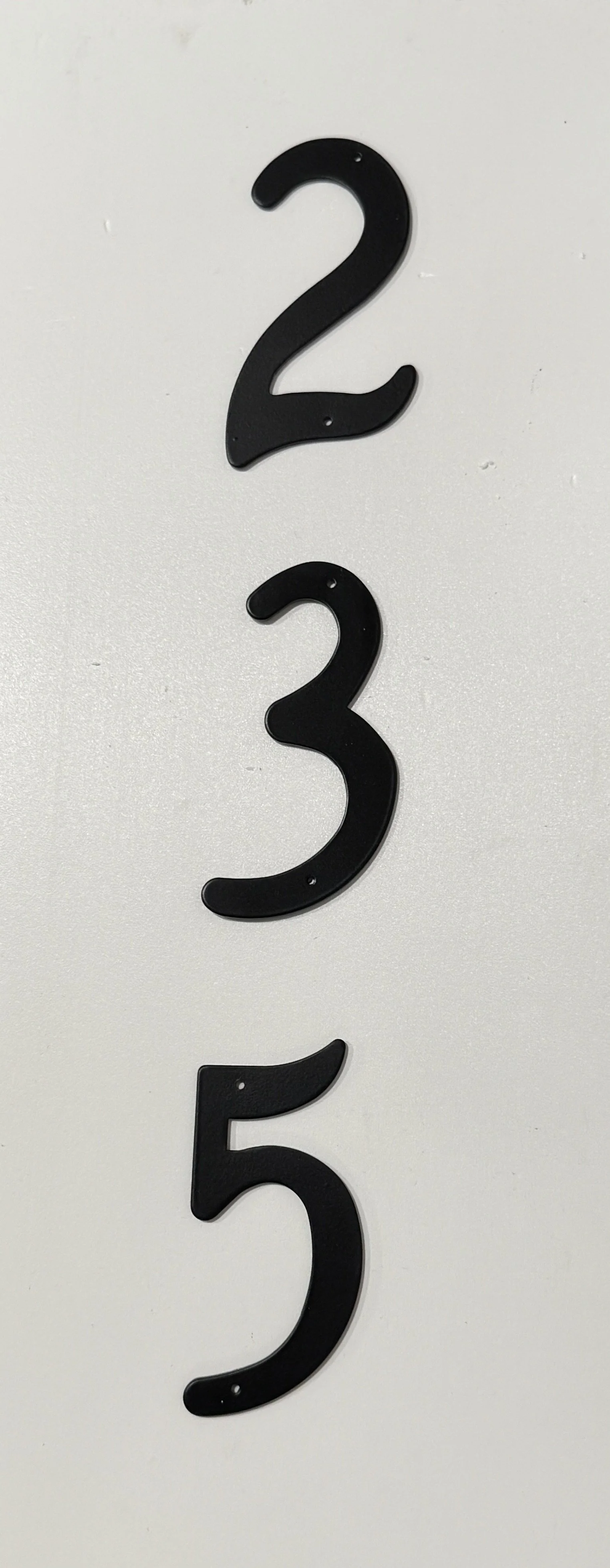 Three black plastic numbers, 2, 3, and 5, mounted vertically on a white wall.