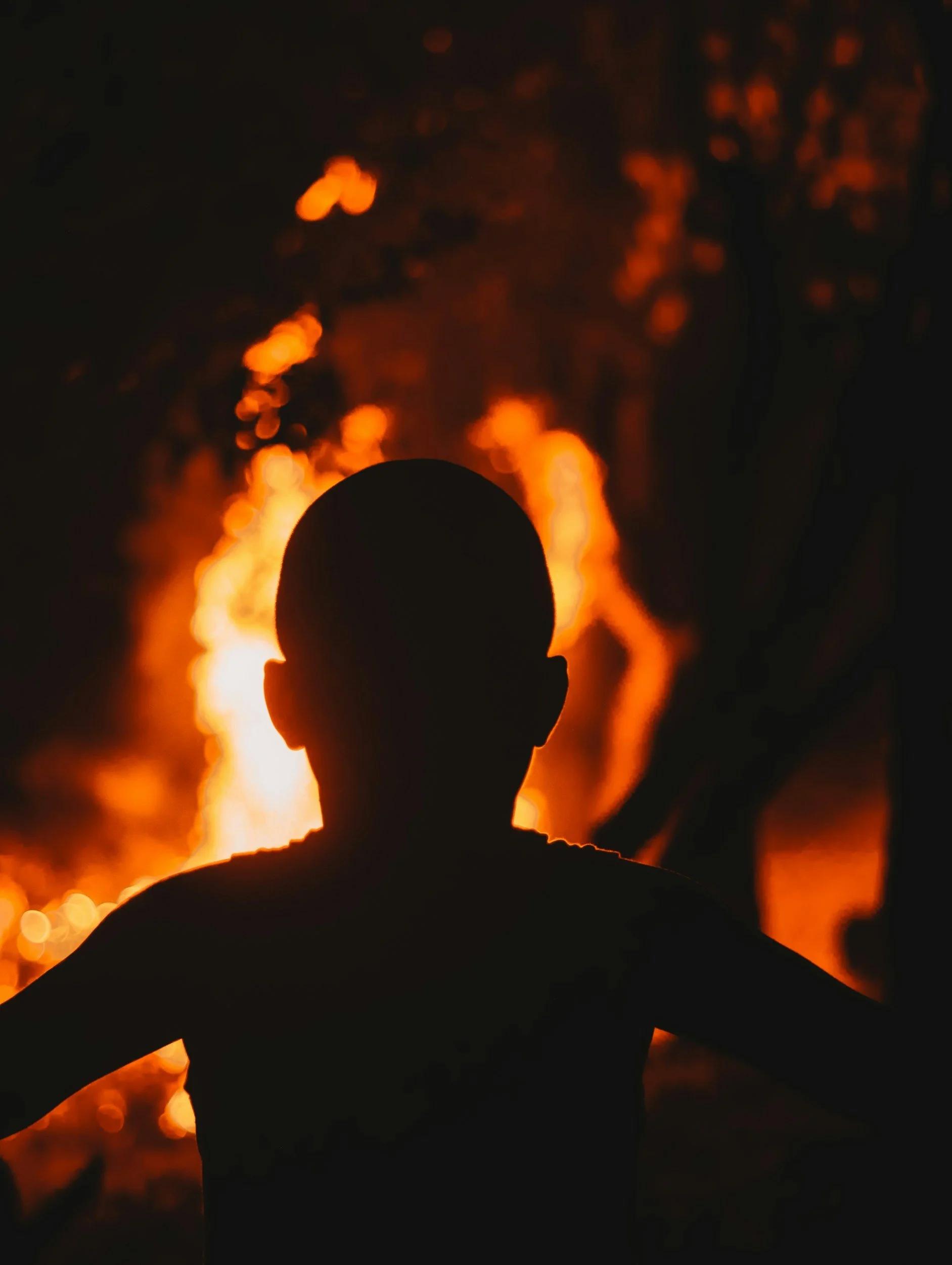 Silhouette of a person watching a large bonfire at night.