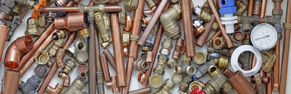 A collection of various plumbing fittings and pipes, including brass, copper, and plastic components, along with a pressure gauge.