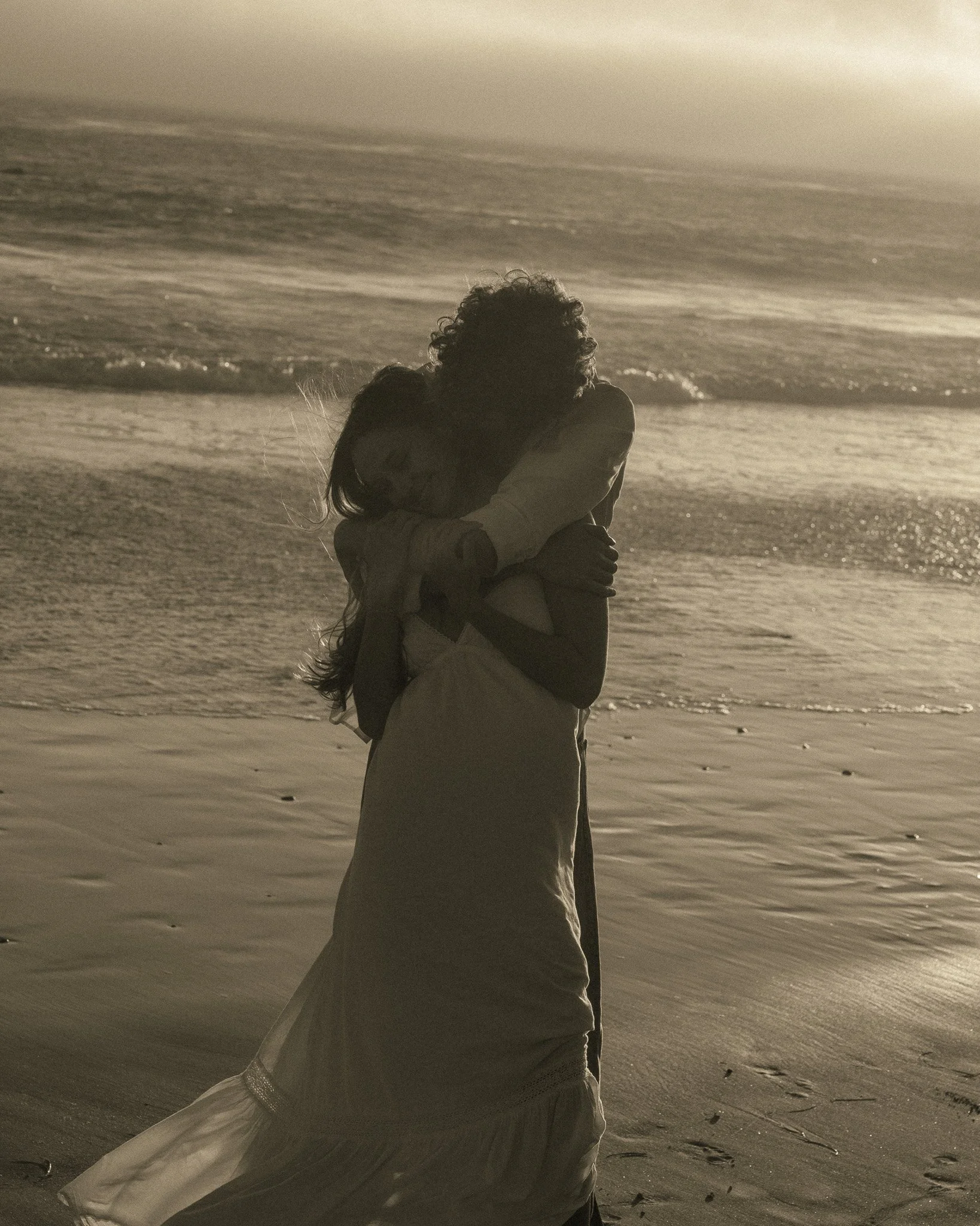 A couple embracing on a beach with waves in the background, captured during sunset or sunrise.