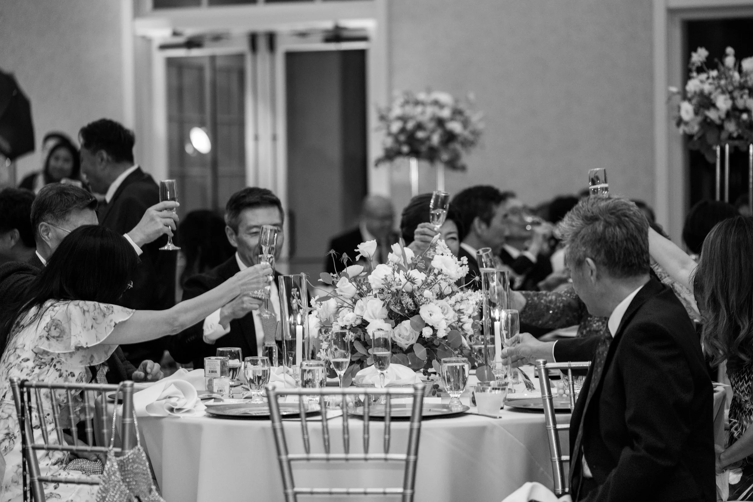 People seated at a decorated banquet table raising glasses in a toast at a formal event or celebration.