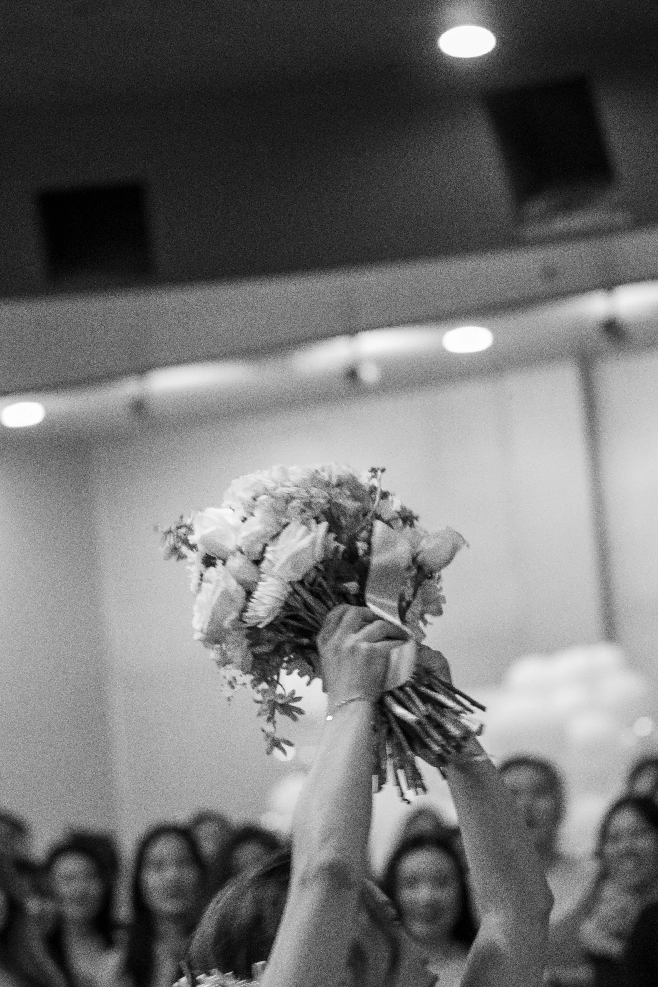 Person holding a bouquet of flowers in front of a group of people, all raising their hands in celebration.