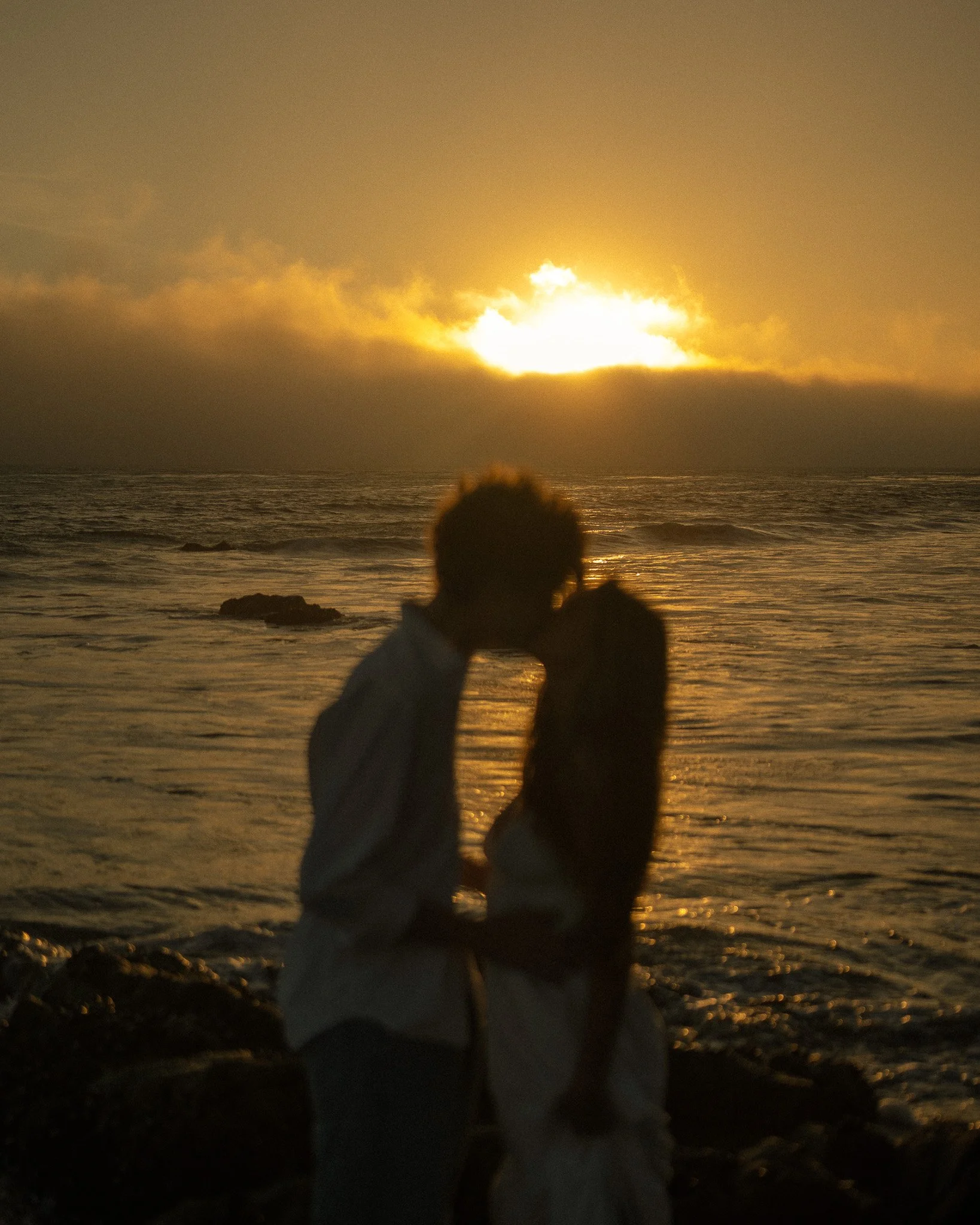 Sunset on the ocean with silhouetted person and rocks in the foreground.