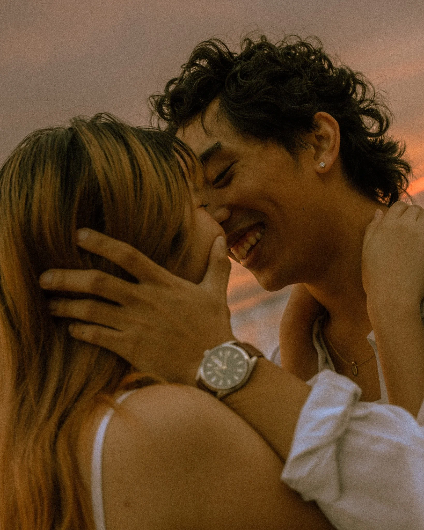 Two people are sharing an intimate moment, with their foreheads touching and eyes closed, in a warm ambient setting.
