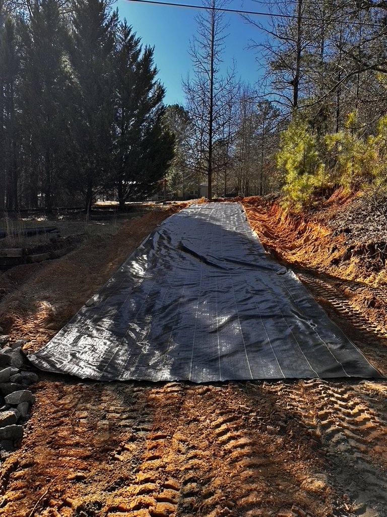 Geotextile fabric placement along freshly graded soil base to stabilize subgrade before gravel installation by ASG Dirtworx.