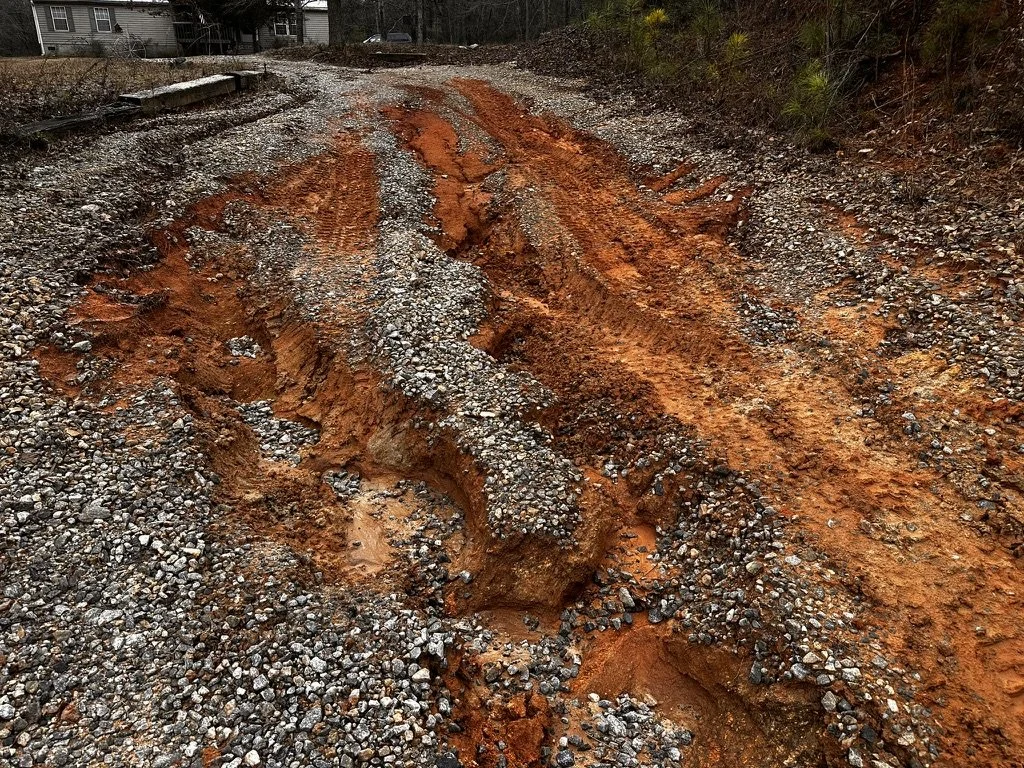 Close-up of deep ruts and gravel displacement from water runoff on an unmaintained driveway before ASG Dirtworx repair and regrading.