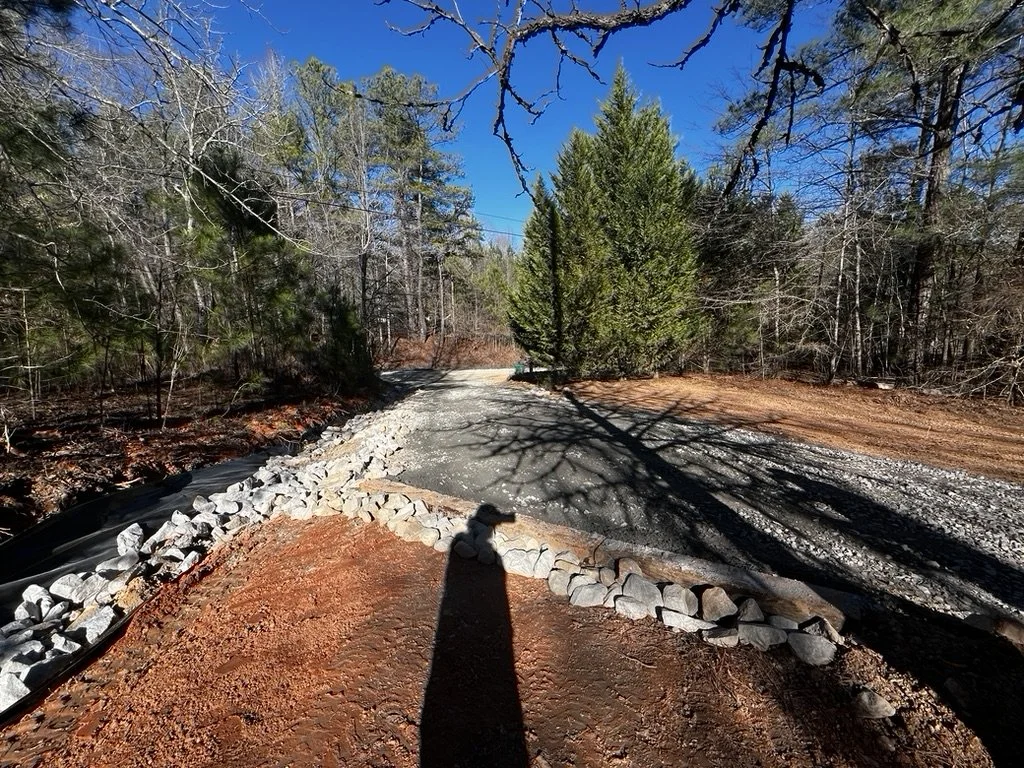 Erosion control measures and gravel installation visible along the newly shaped driveway slope, completed by ASG Dirtworx.