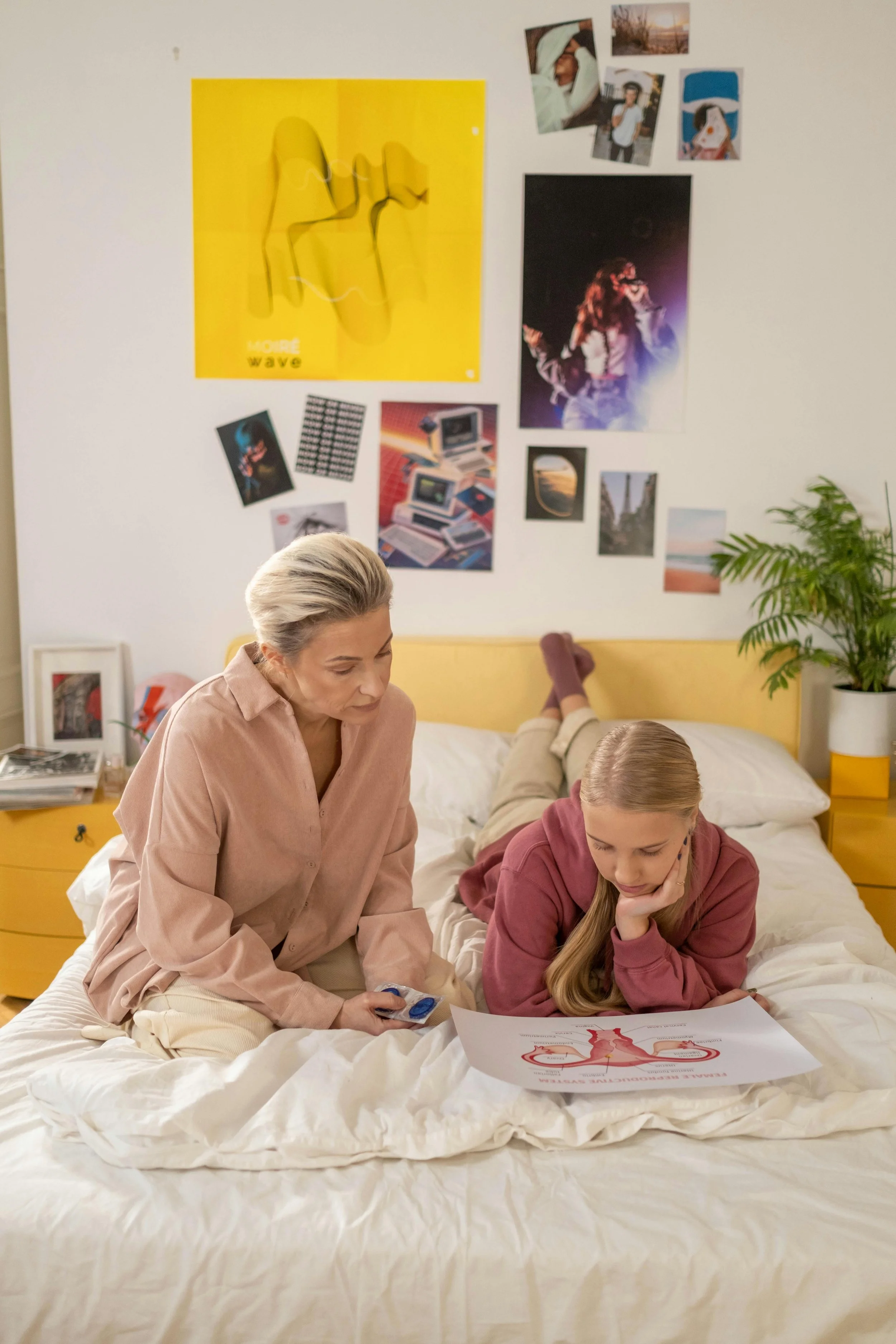 Une femme plus âgée et une jeune fille, mère et fille, sont assises sur un lit dans une chambre moderne. a fille regarde un poster avec un diagramme de cycle.
