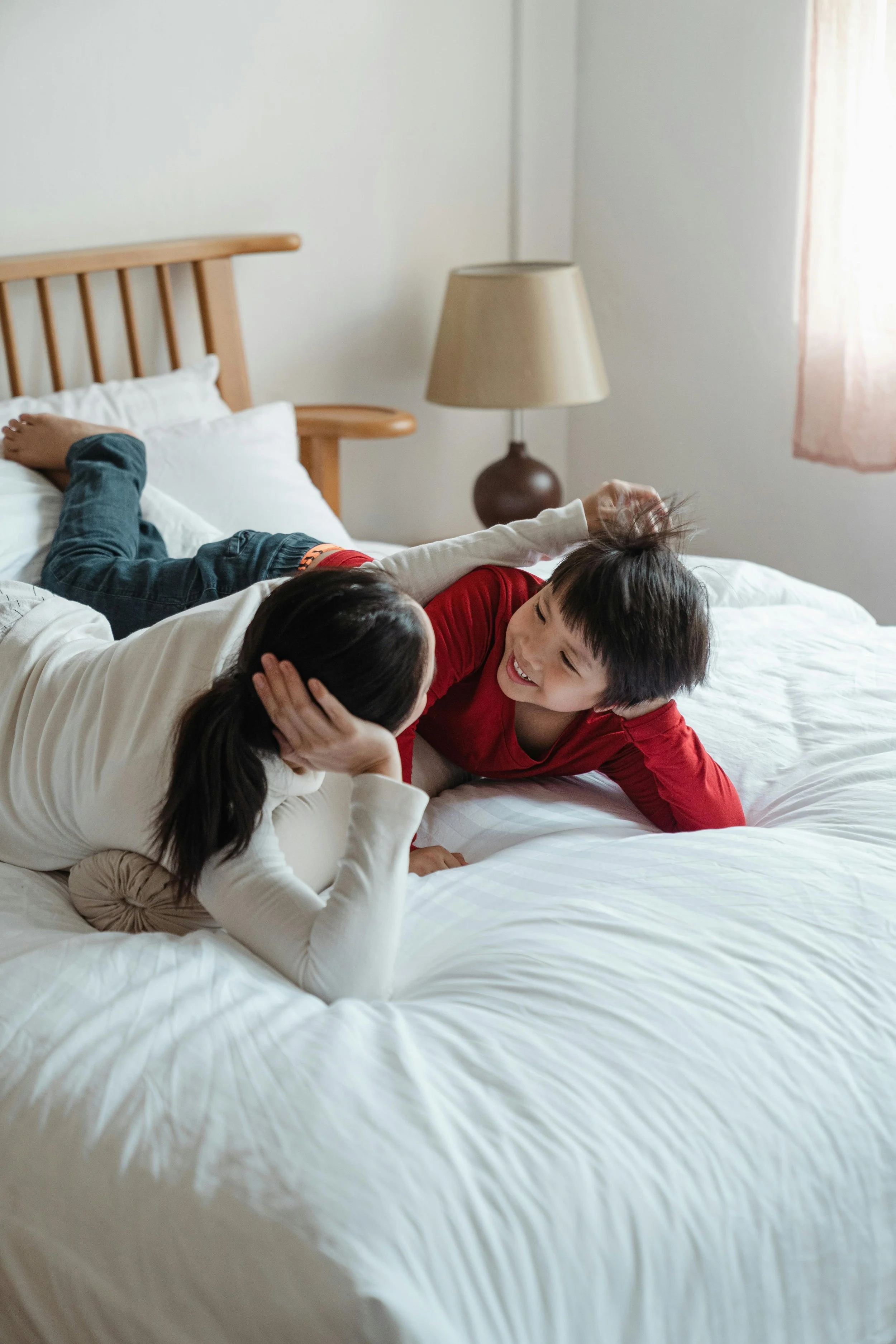 Deux enfants jouant et riant sur un lit dans une chambre. Un enfant en chemise blanche et autre en t-shirt rouge. Commeorie et ambiance joyeuse.