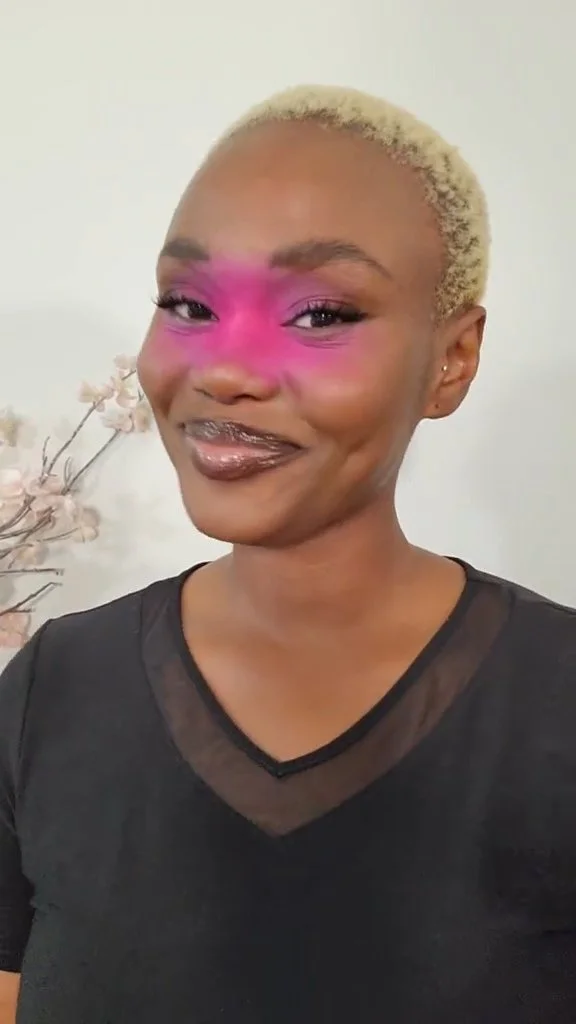 Hilary Biaku | Black Female Model, Creative Strategist, Content Creator, Public Speaker, and Life Coach —  A woman with short blonde hair, wearing black clothing, has pink makeup over her eyes and smiling.