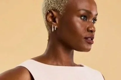 Hilary Biaku | Black Female Model, Creative Strategist, Content Creator, Public Speaker, and Life Coach — A woman with short, platinum blonde hair, wearing hoop earrings, looking to the right, against a beige background.