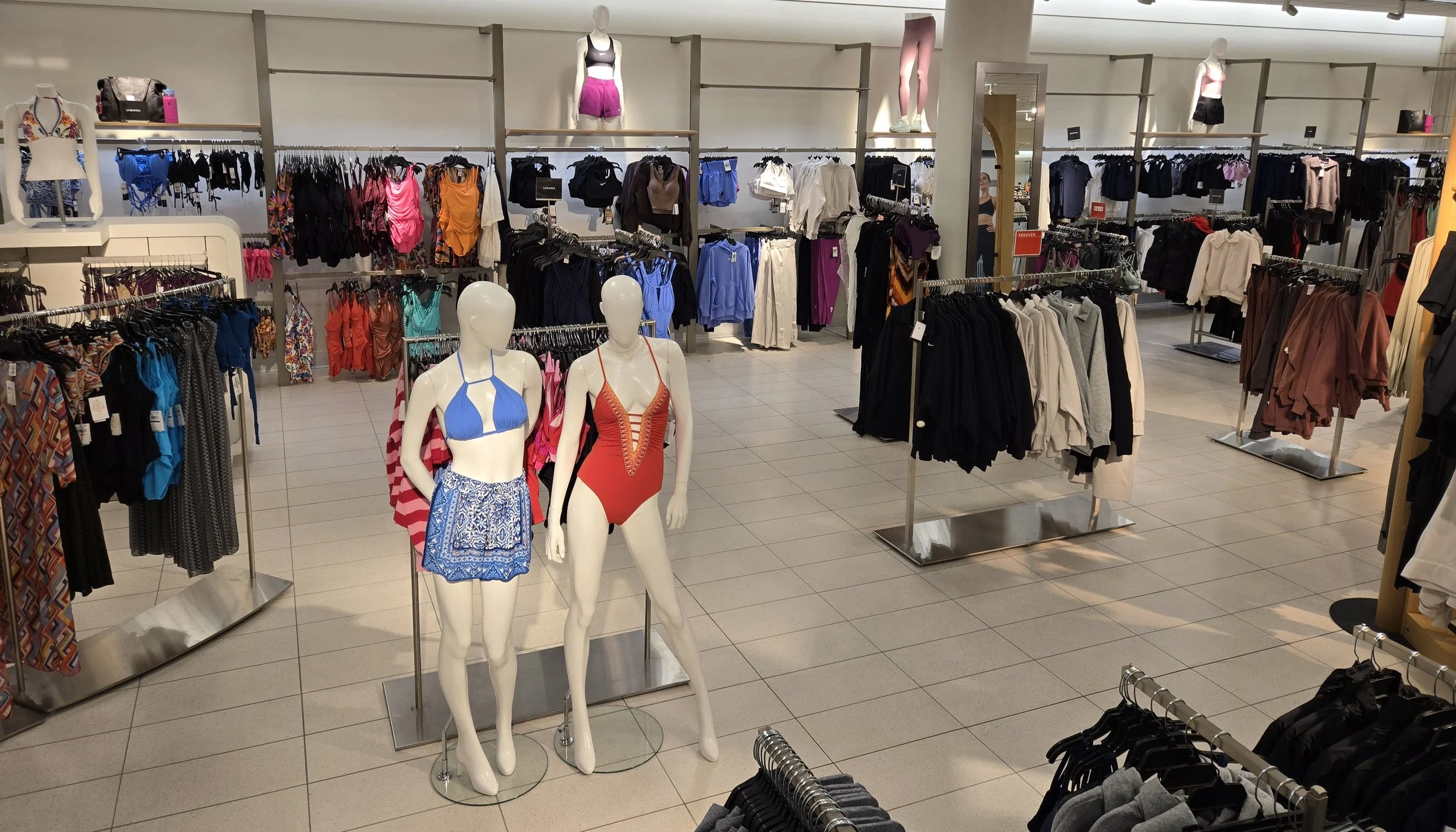 Hilary Biaku | Black Female Model, Creative Strategist, Content Creator, Public Speaker, and Life Coach —  Mannequins wearing swimsuits in a clothing store, surrounded by racks of clothes including shorts, tops, and jackets.
