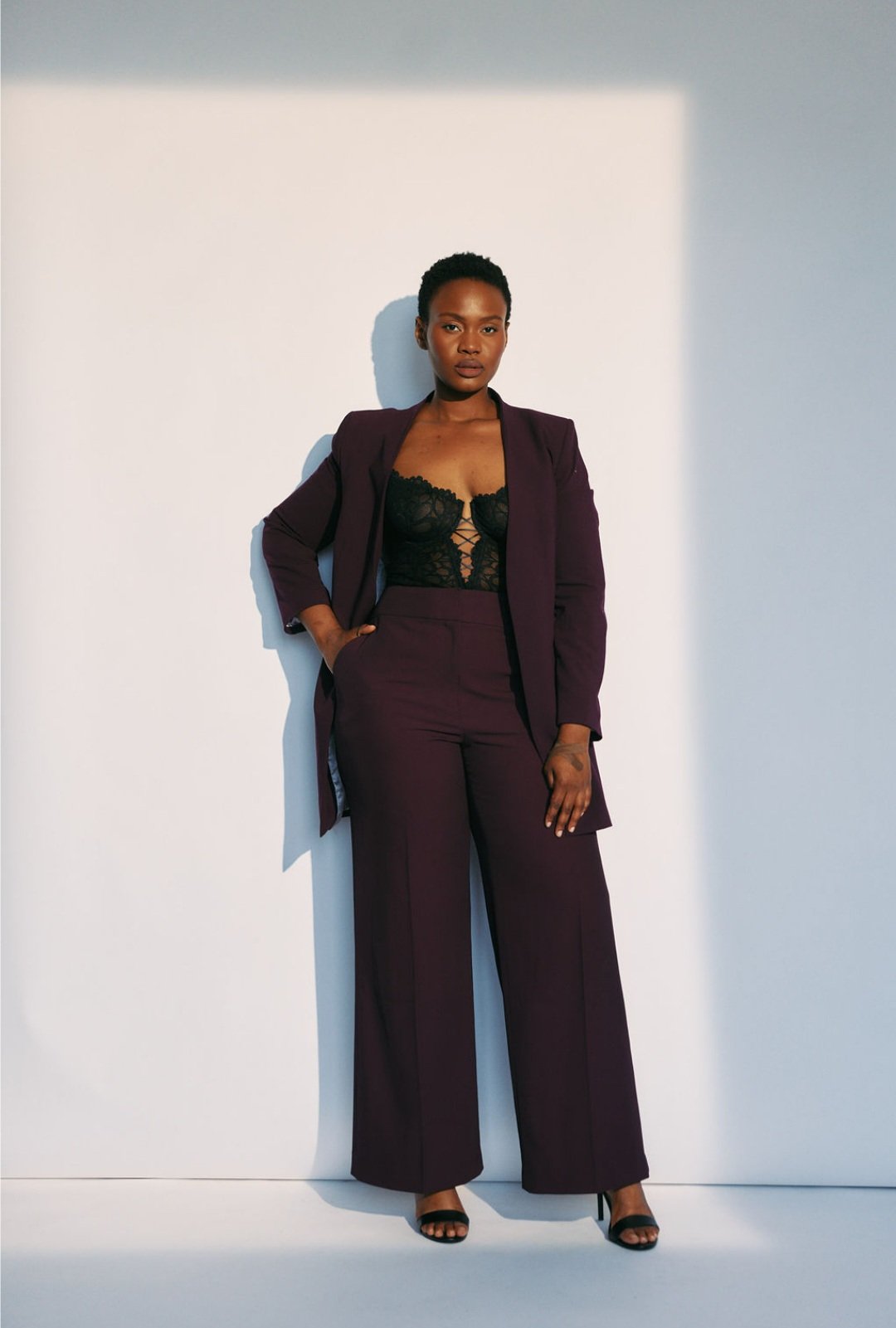 Hilary Biaku | Black Female Model, Creative Strategist, Content Creator, Public Speaker, and Life Coach — A woman wearing a maroon suit with a black lace top, standing against a plain white background.
