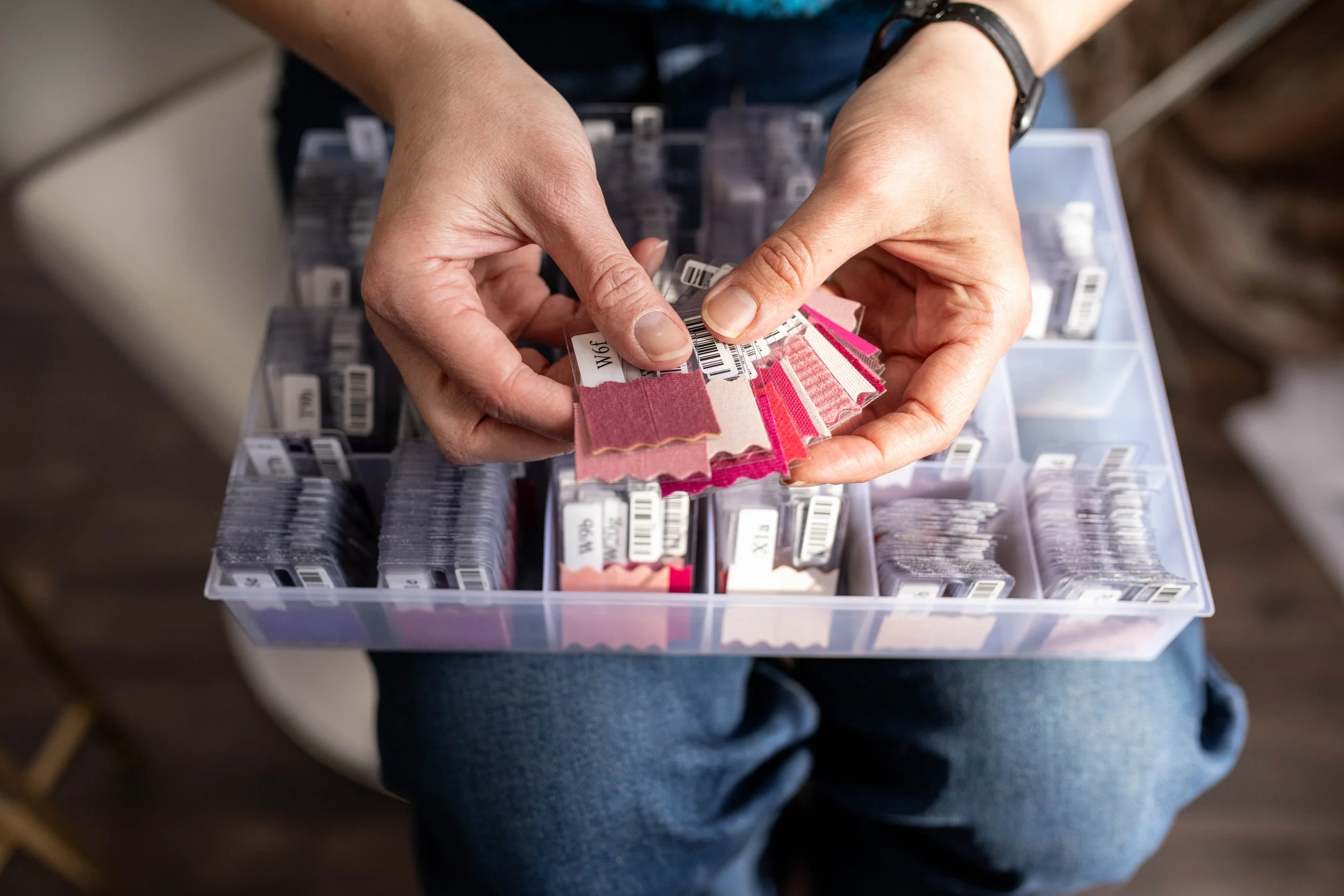 Person holding color analysis fabric swatches in front of a plastic storage container filled with fabric sample strips.