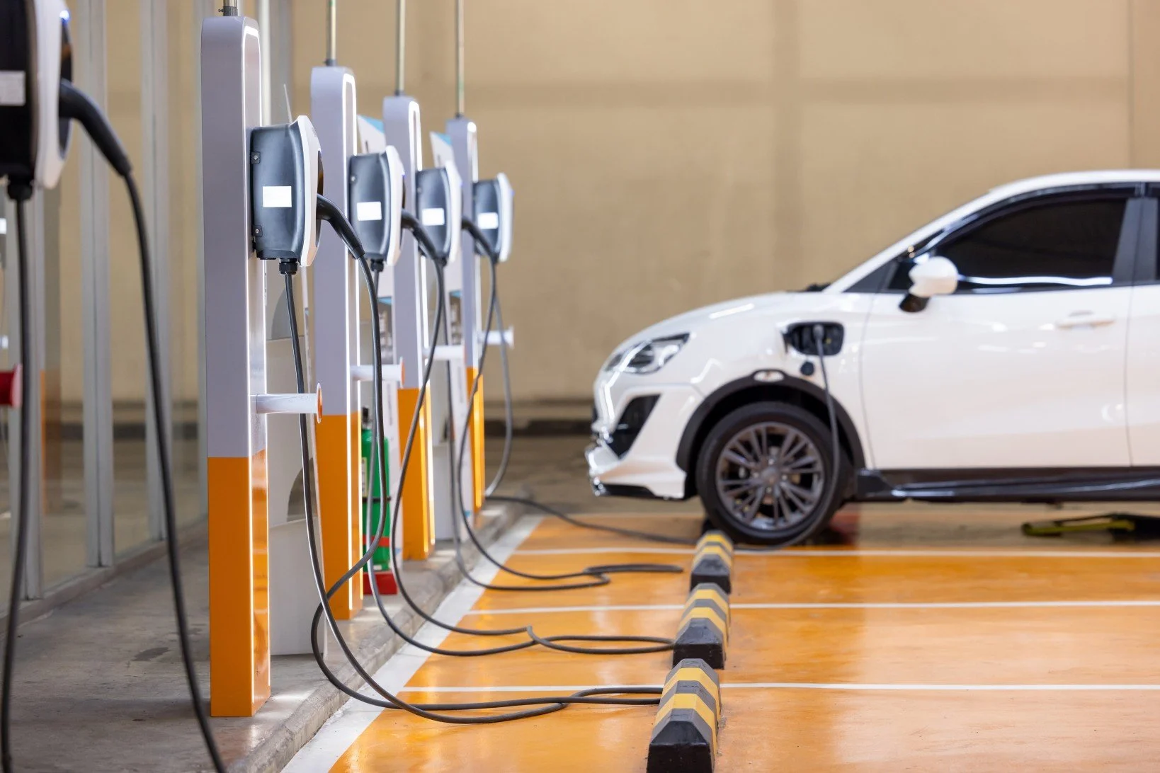 Electric white car charging at an EV charging station inside a parking garage.