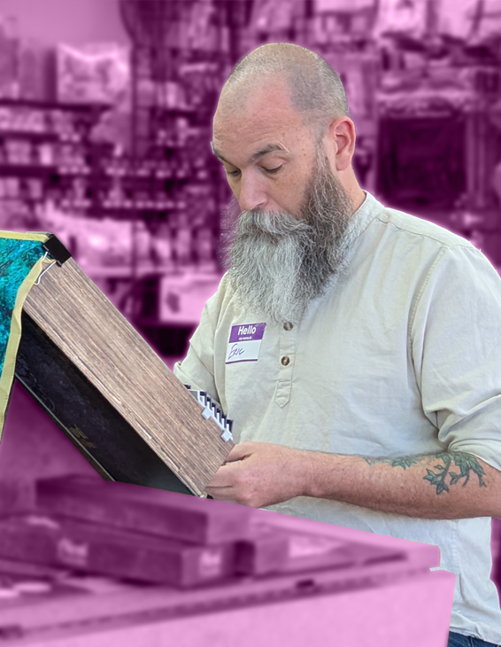 A man with a beard and tattooed arm shopping for books in a store, with shelves full of books in the background.