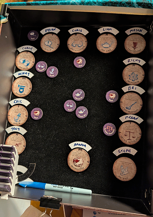 Board game setup with cork and purple game pieces labeled with names and roles, including character and profession titles.