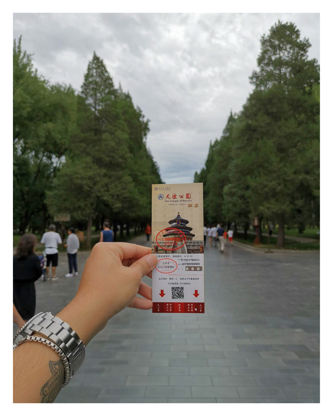 Person holding a ticket for The Temple of Heaven in Beijing, with trees and visitors in the background.