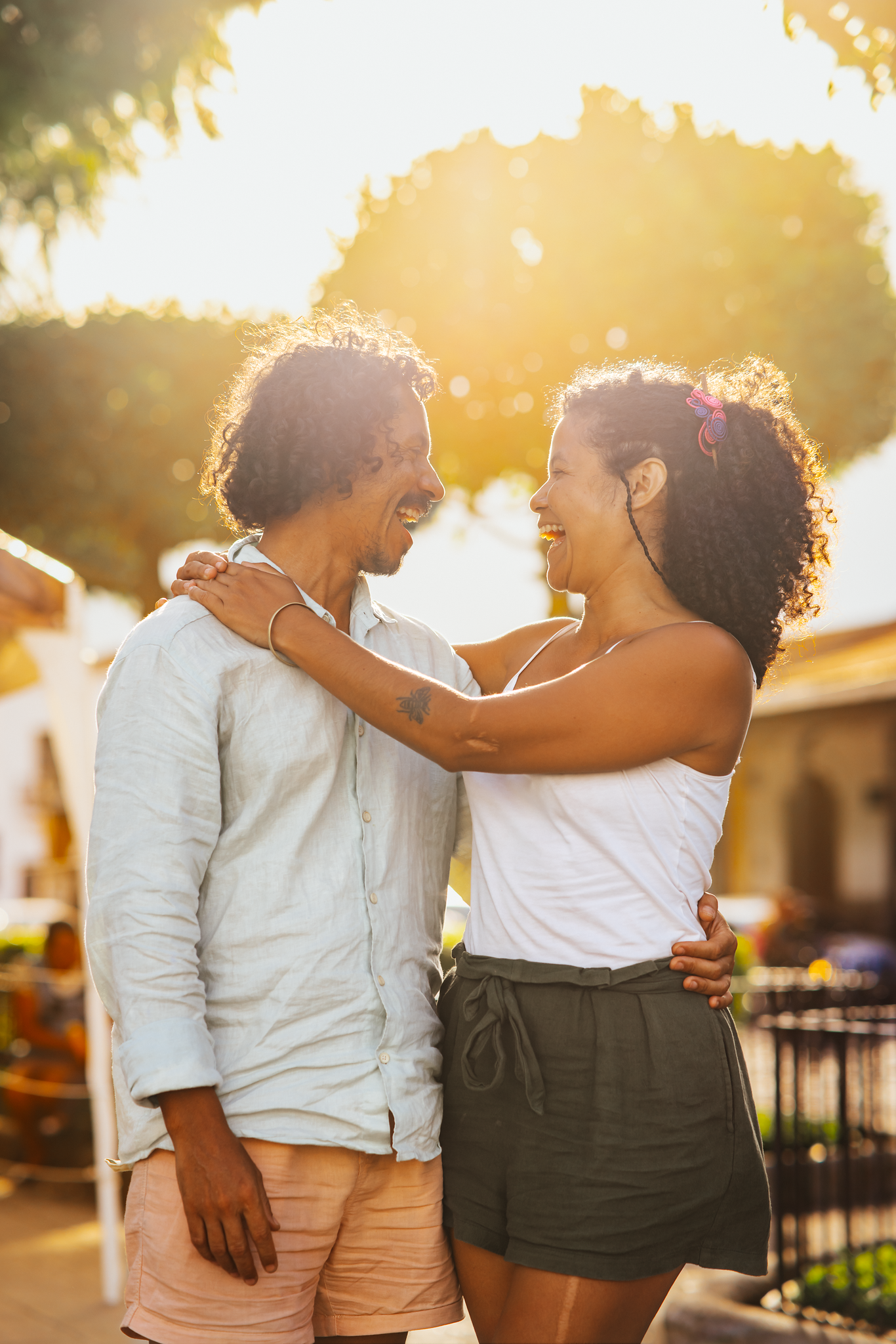 A man and woman are smiling and embracing outdoors during sunset.