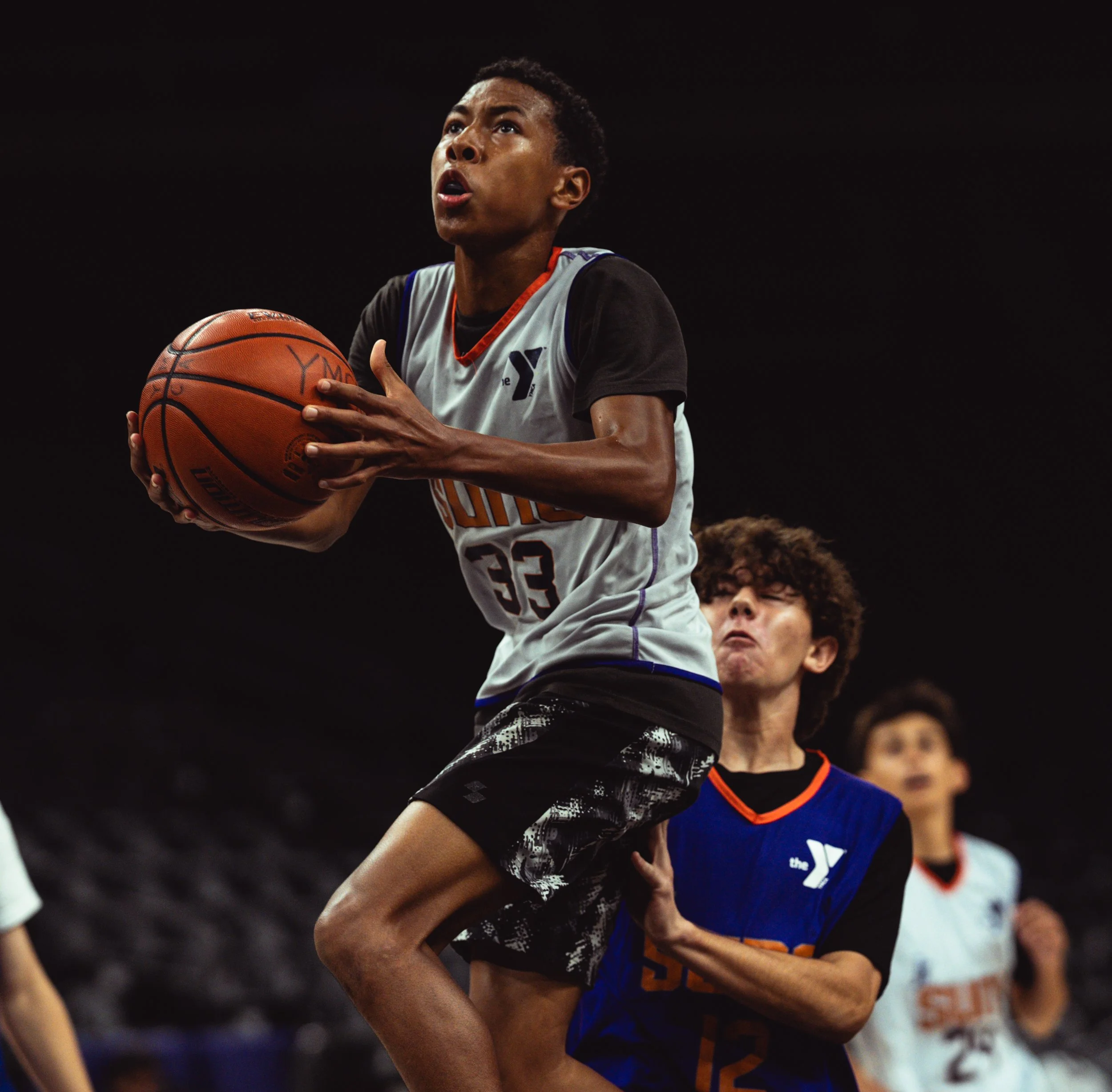 A young basketball player with jersey number 33 attempting a shot, guarded by a player with jersey number 12, on an indoor court.
