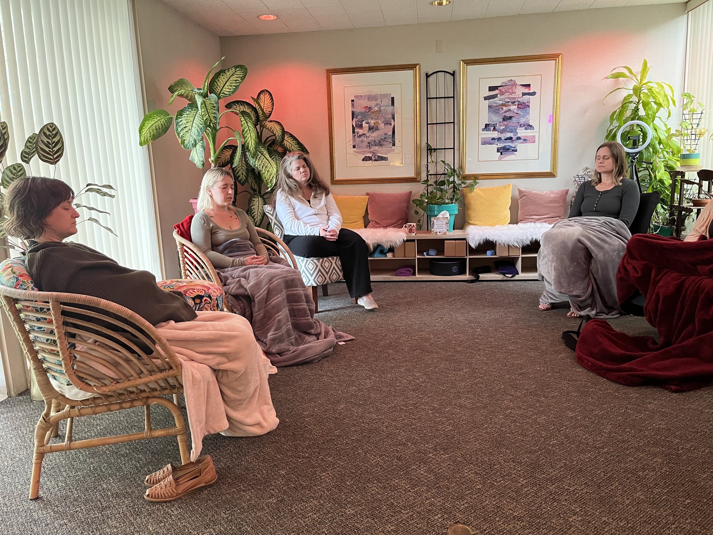 People meditating in a cozy room filled with plants and artwork.
