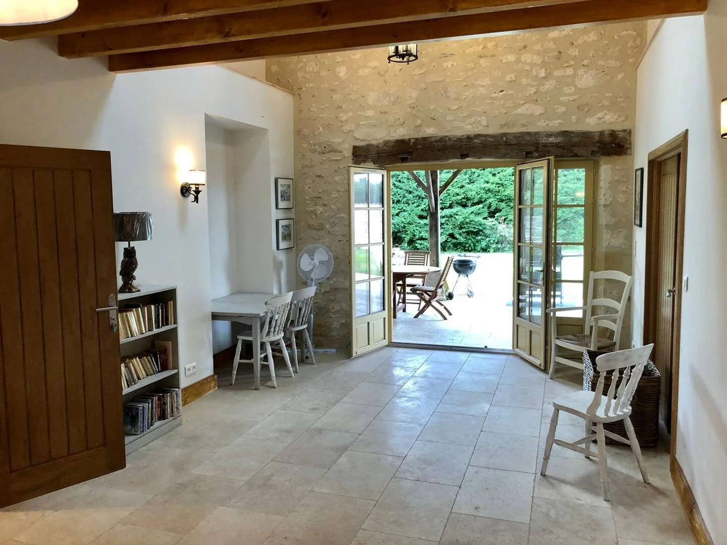 Living room with open French doors leading to an outdoor patio with trees and outdoor furniture.