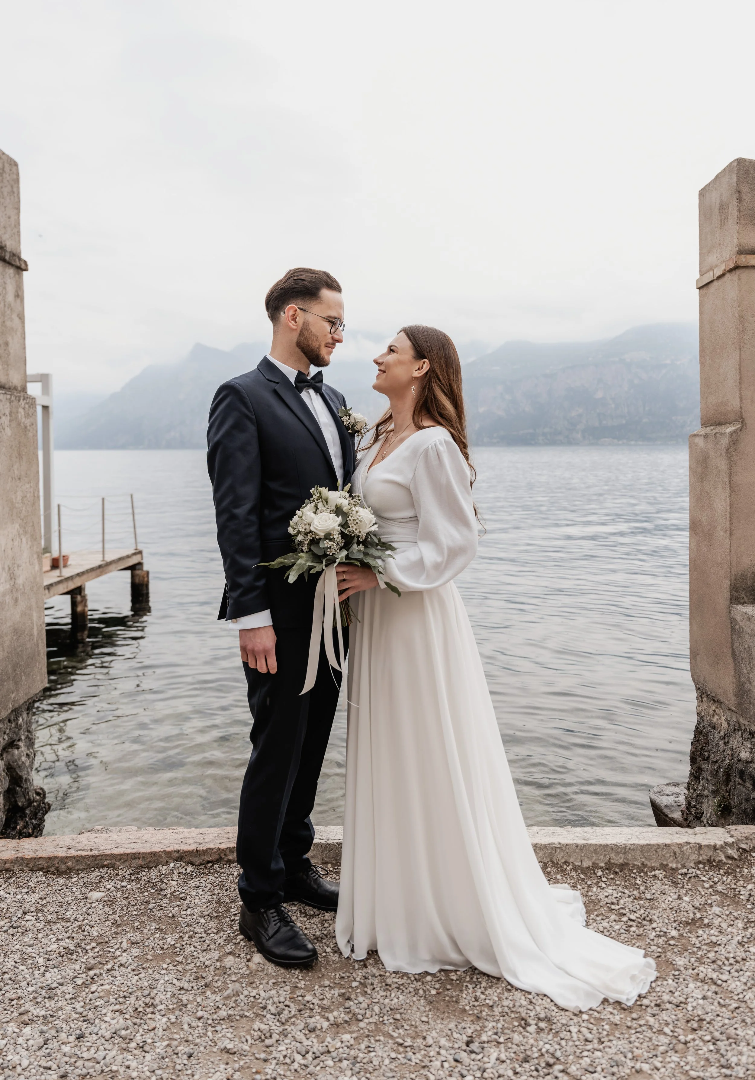 Ein Brautpaar steht sich vor einem See und schaut sich liebevoll an, umgeben von Bergen, bei einer Hochzeit im Freien.
