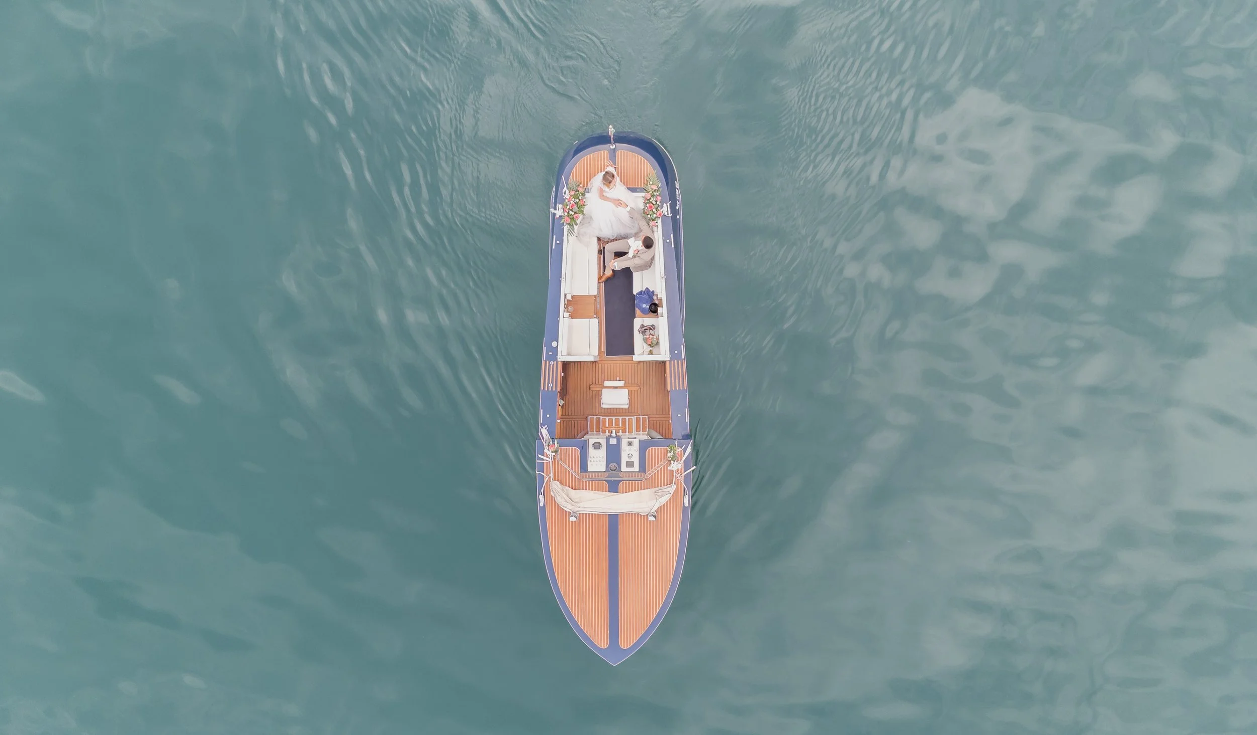Vogelperspektive auf ein Boot mit einer Hochzeitspartei, das auf ruhigem Wasser fährt.
Destination Wedding Photographer
