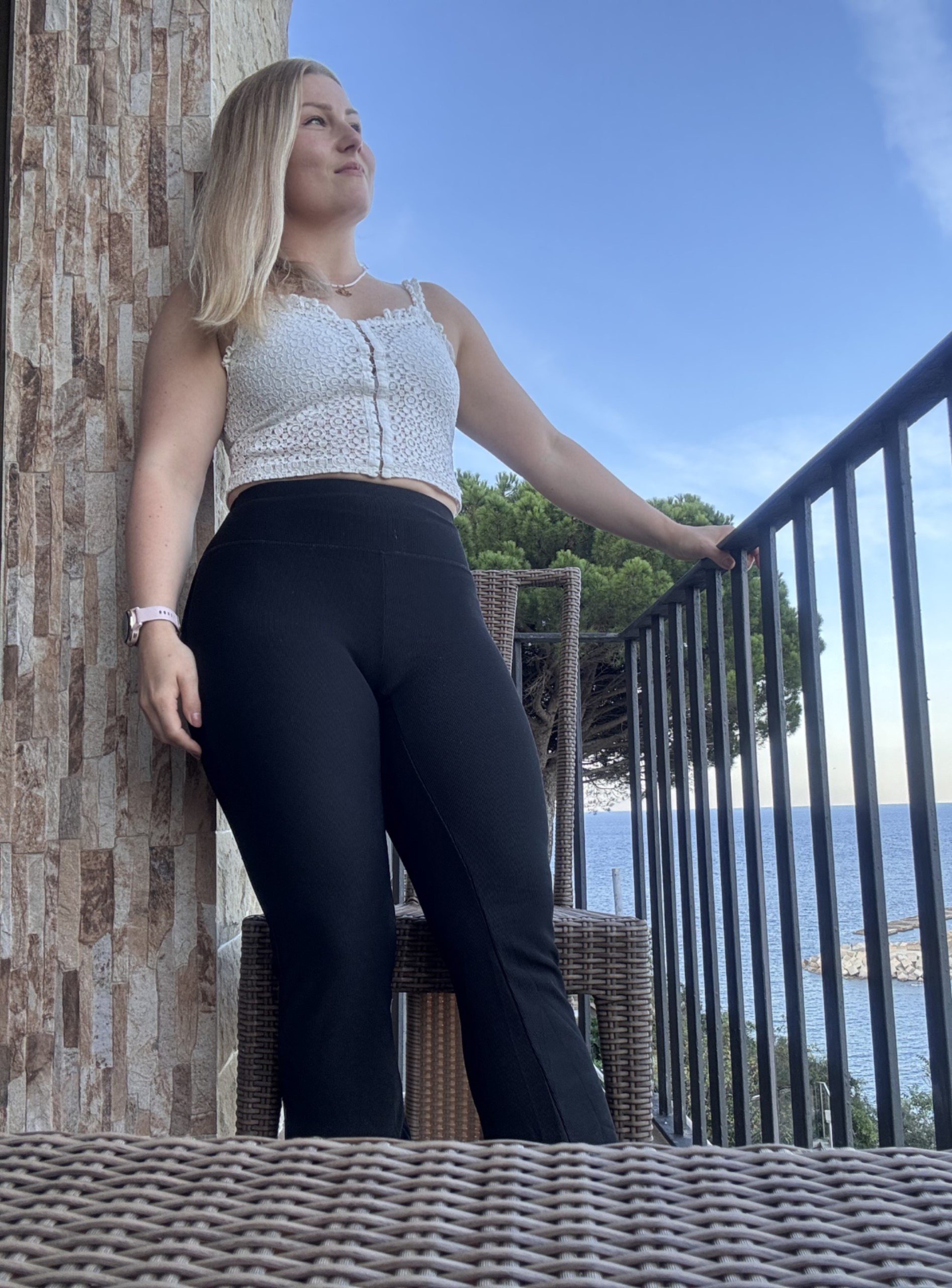 Nuori nainen seisoo rantatontilla, katsoo horisonttiin, meren ja taivaan näkyvissä taustalla.