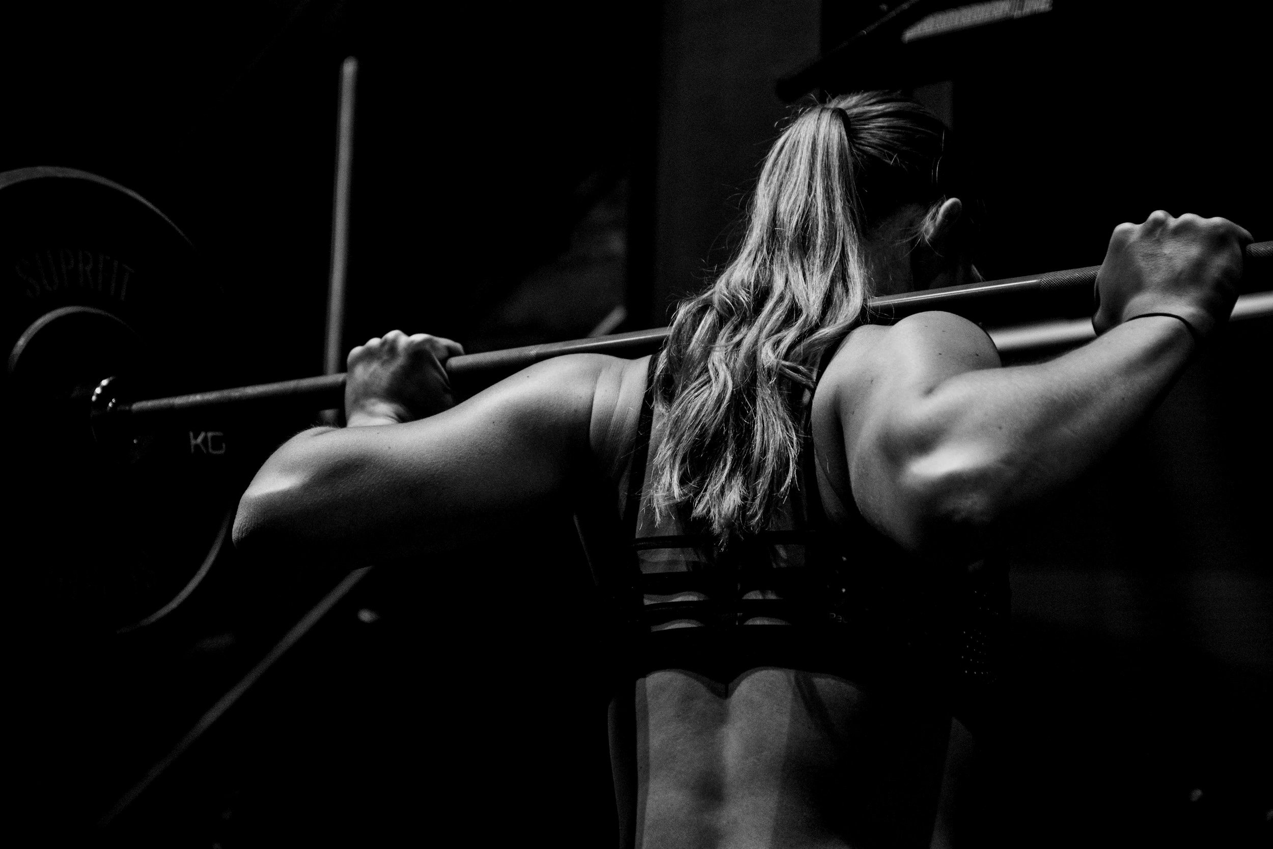 Mustavalkoinen kuva naisesta nostamassa tankoa harteillaan salilla.