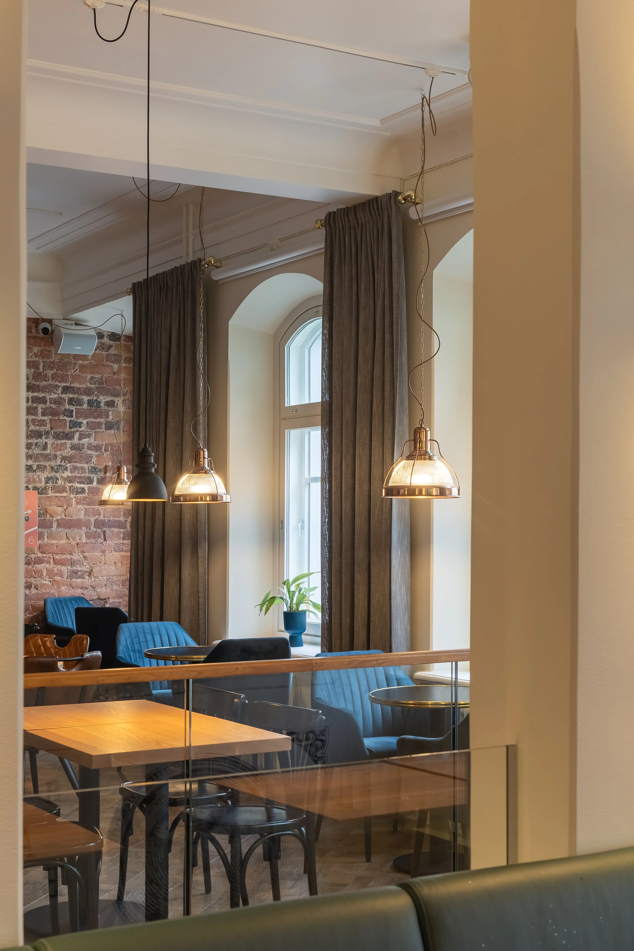 Kahvilan tai ravintolan sisustus, joissa on puisia pöytiä ja sinisiä nojatuoleja, iso ikkunaruudullinen ikkuna ja roikkuvat valaisimet.