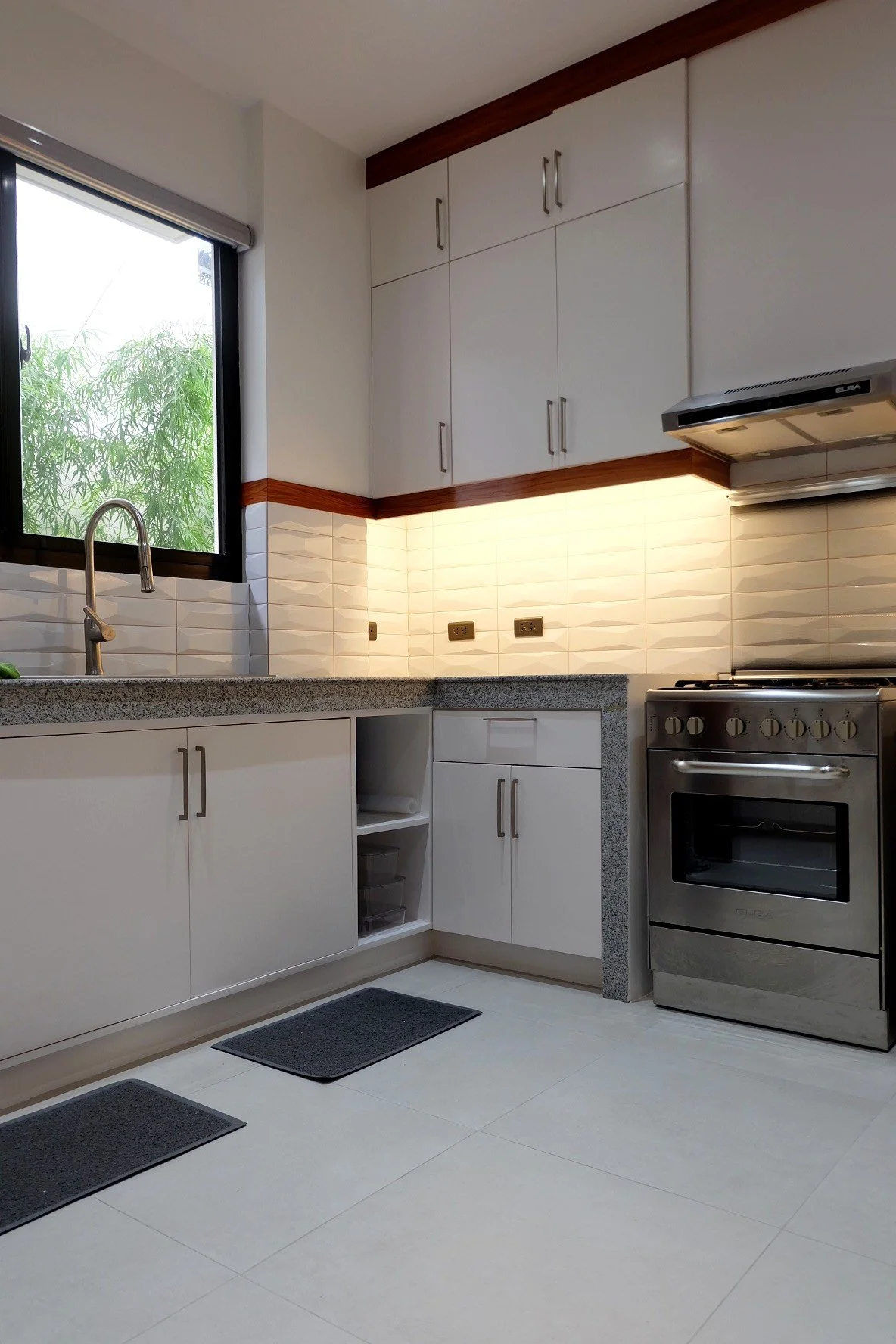 Clean kitchen with white cabinets, gray countertop, stainless steel stove, and window overlooking greenery.