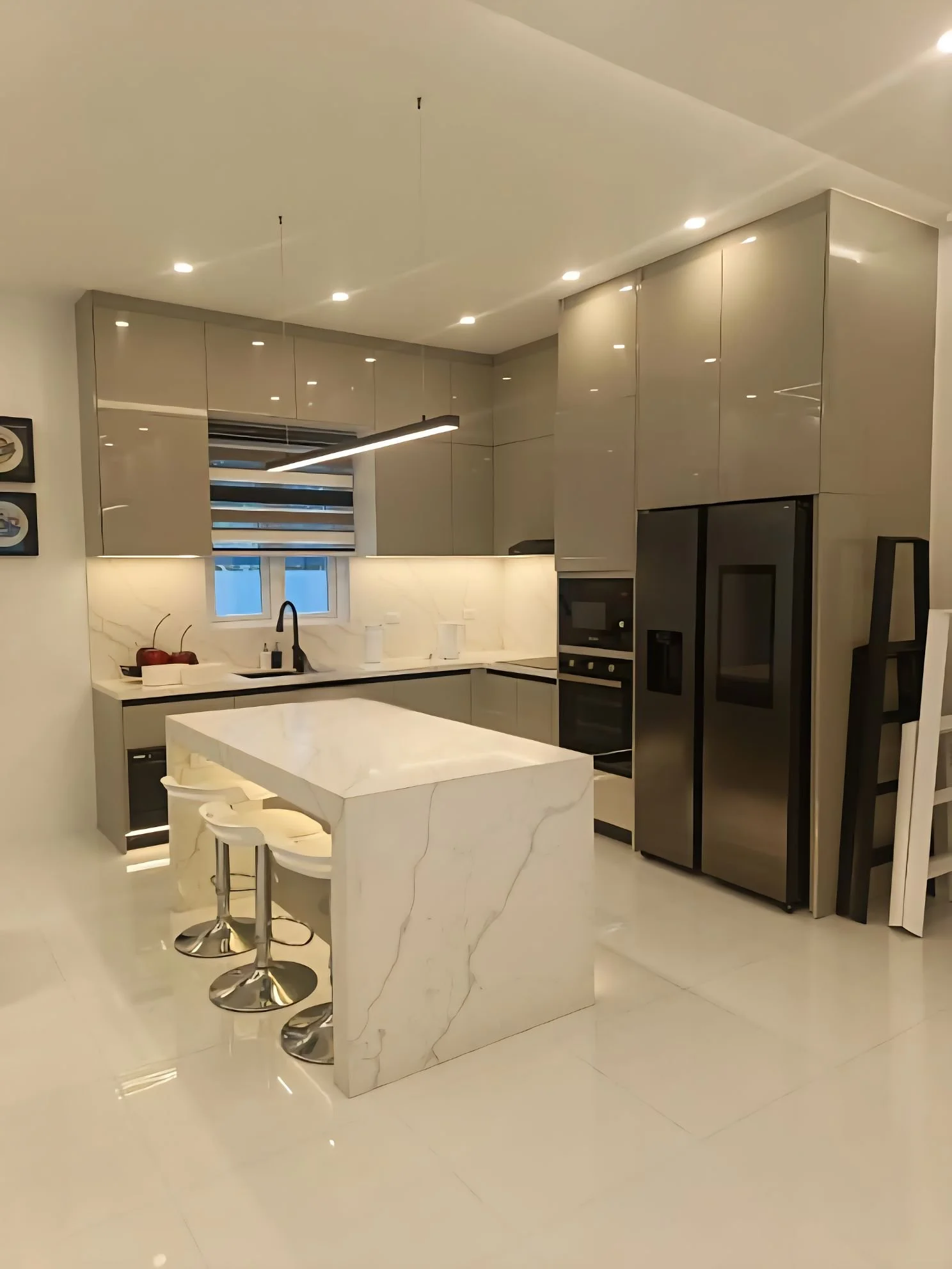 Modern kitchen with glossy gray cabinets, white marble island, built-in oven, refrigerator, and black accents, illuminated by recessed ceiling lights.