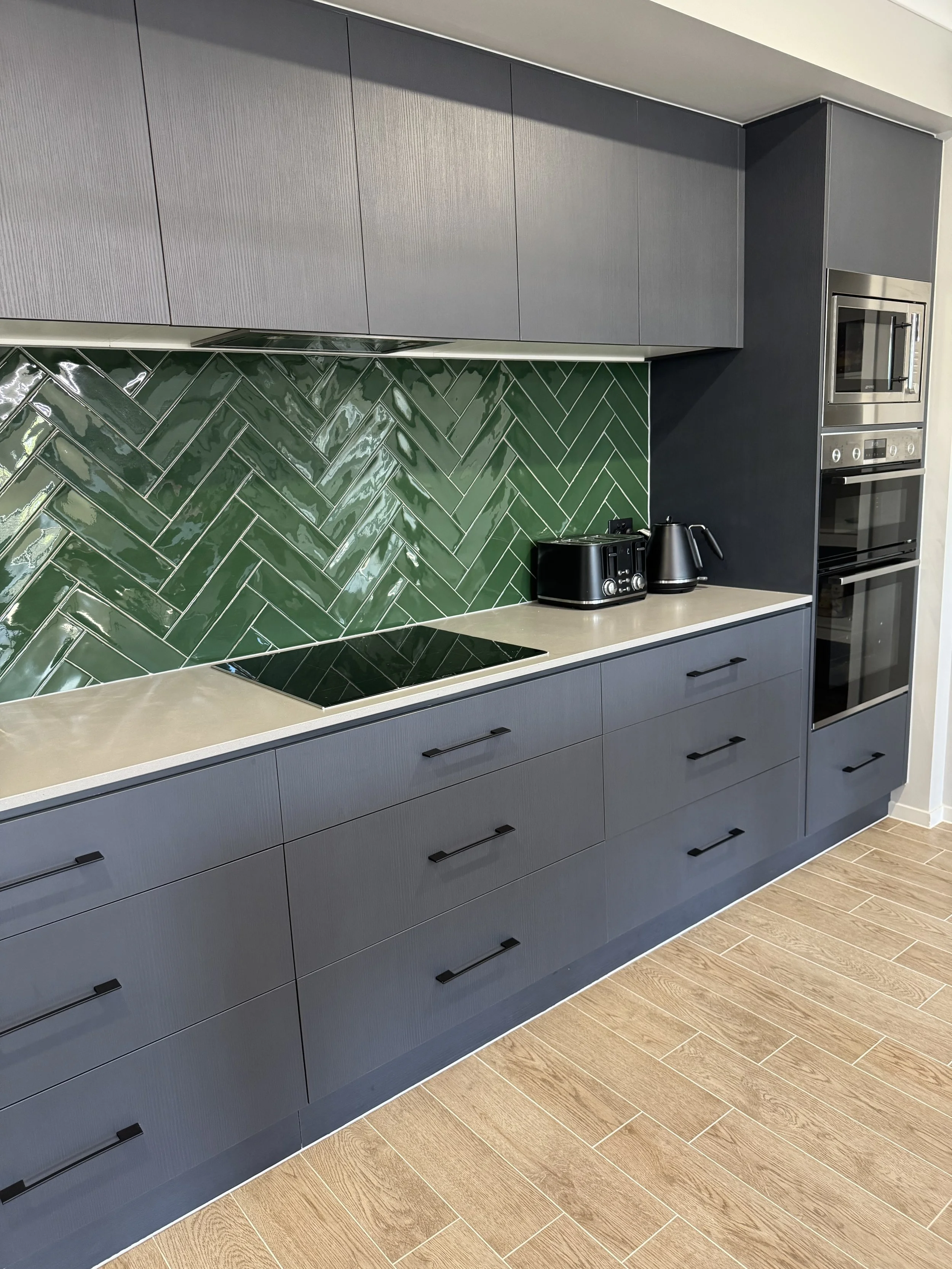Beautiful clean modern kitchen with green tile splash back, cream counter tops and dark grey cupboards