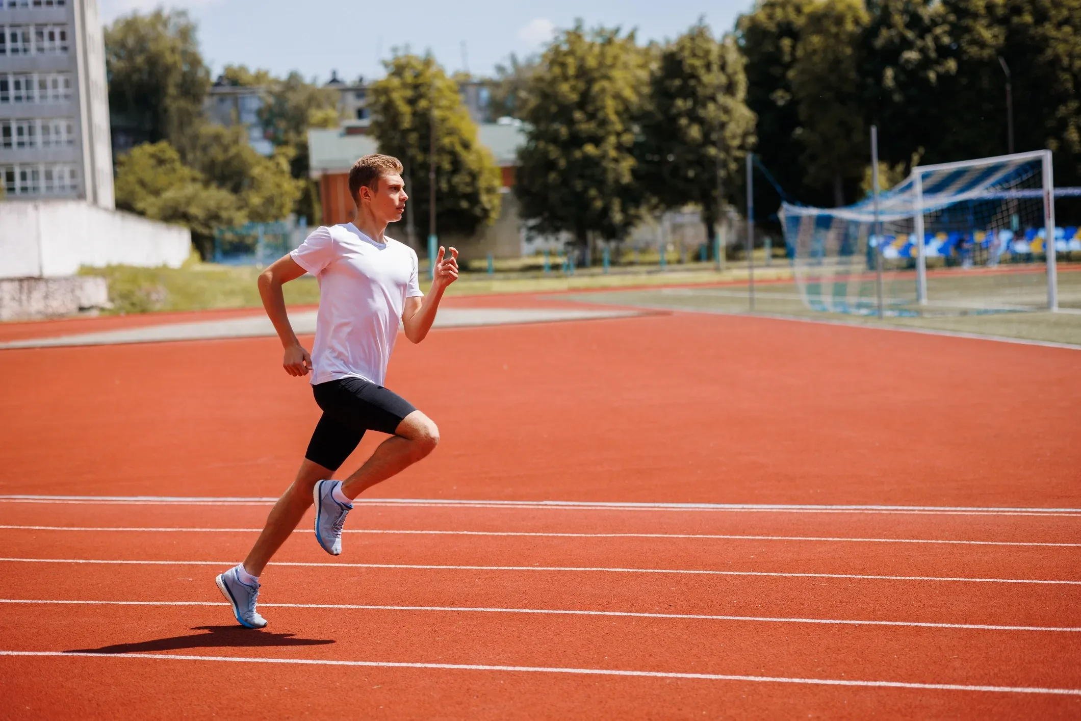 A young man running on a red outdoor athletic track during daytime.