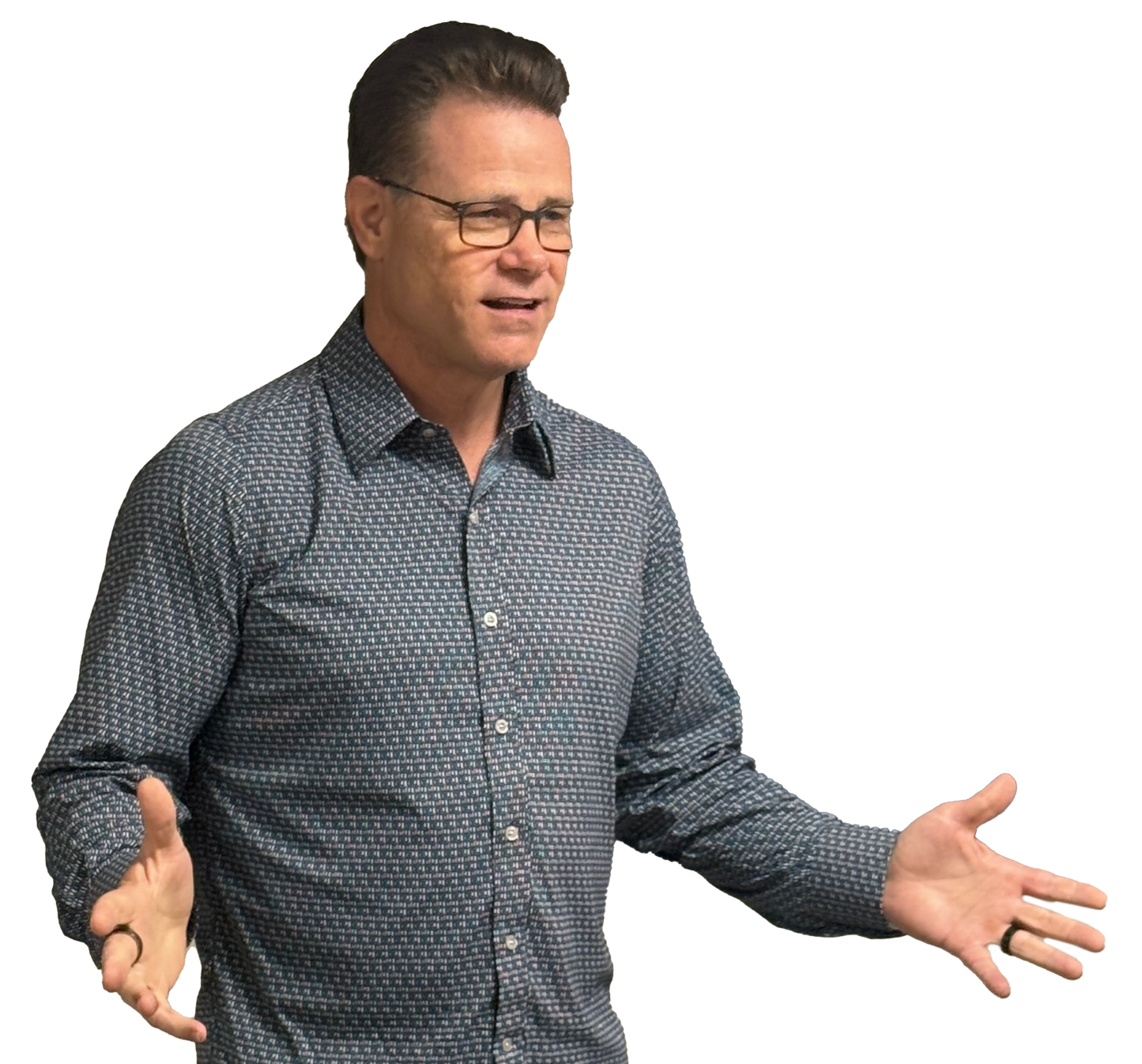 A man with glasses and a patterned shirt gesturing with his hands, appearing to speak or explain something.