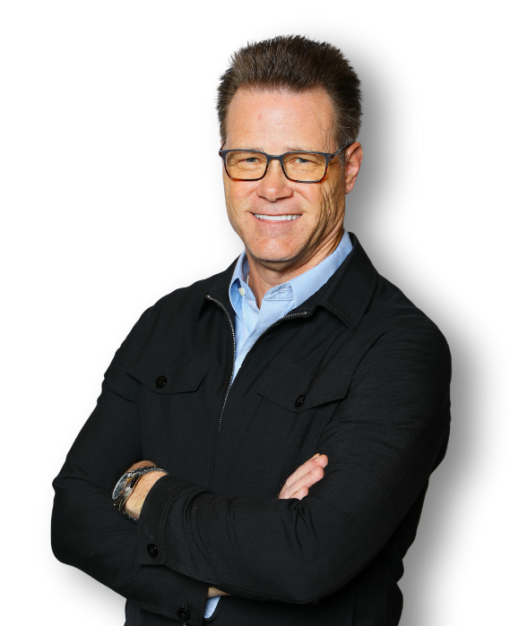 Smiling middle-aged man wearing glasses, a light blue shirt, and a black jacket against a black background.