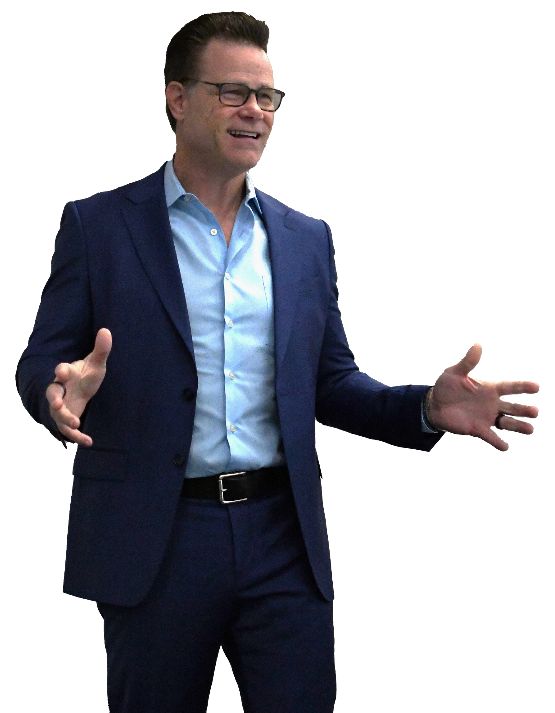 A man wearing glasses and a navy blue suit is gesturing with his hands while speaking, with a blurred colorful background.