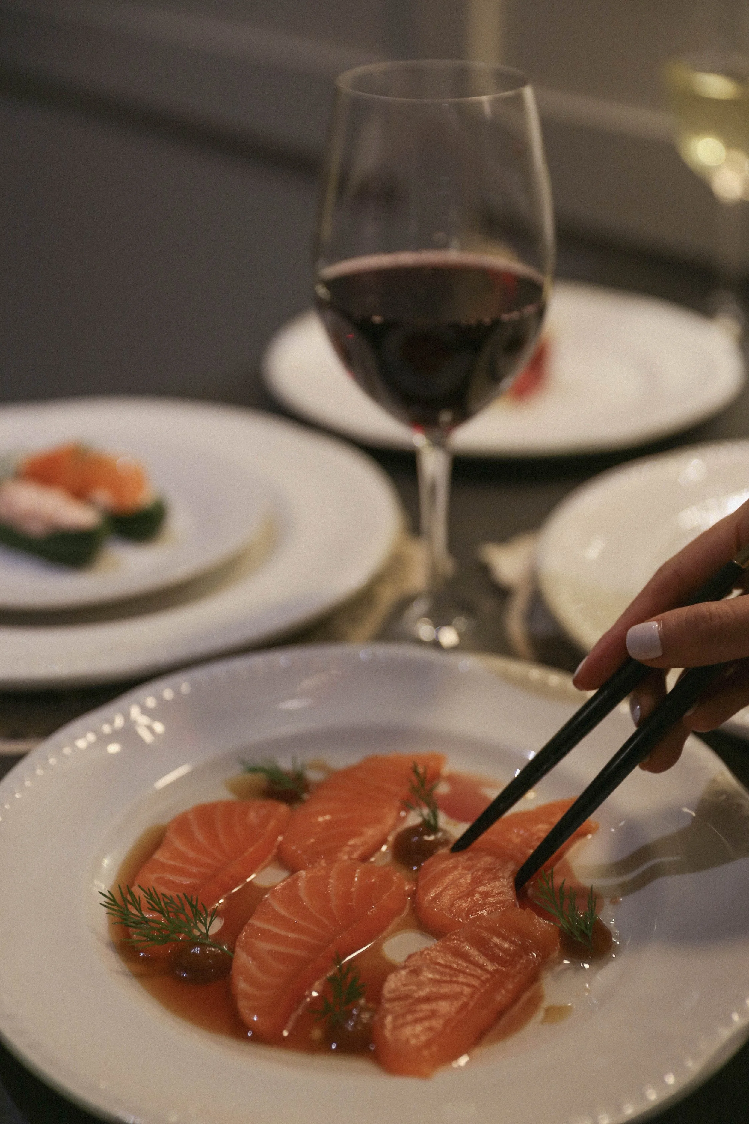 A plate of sliced smoked salmon garnished with dill and capers, in a shallow bowl of vinaigrette or sauce with red wine at a private event.