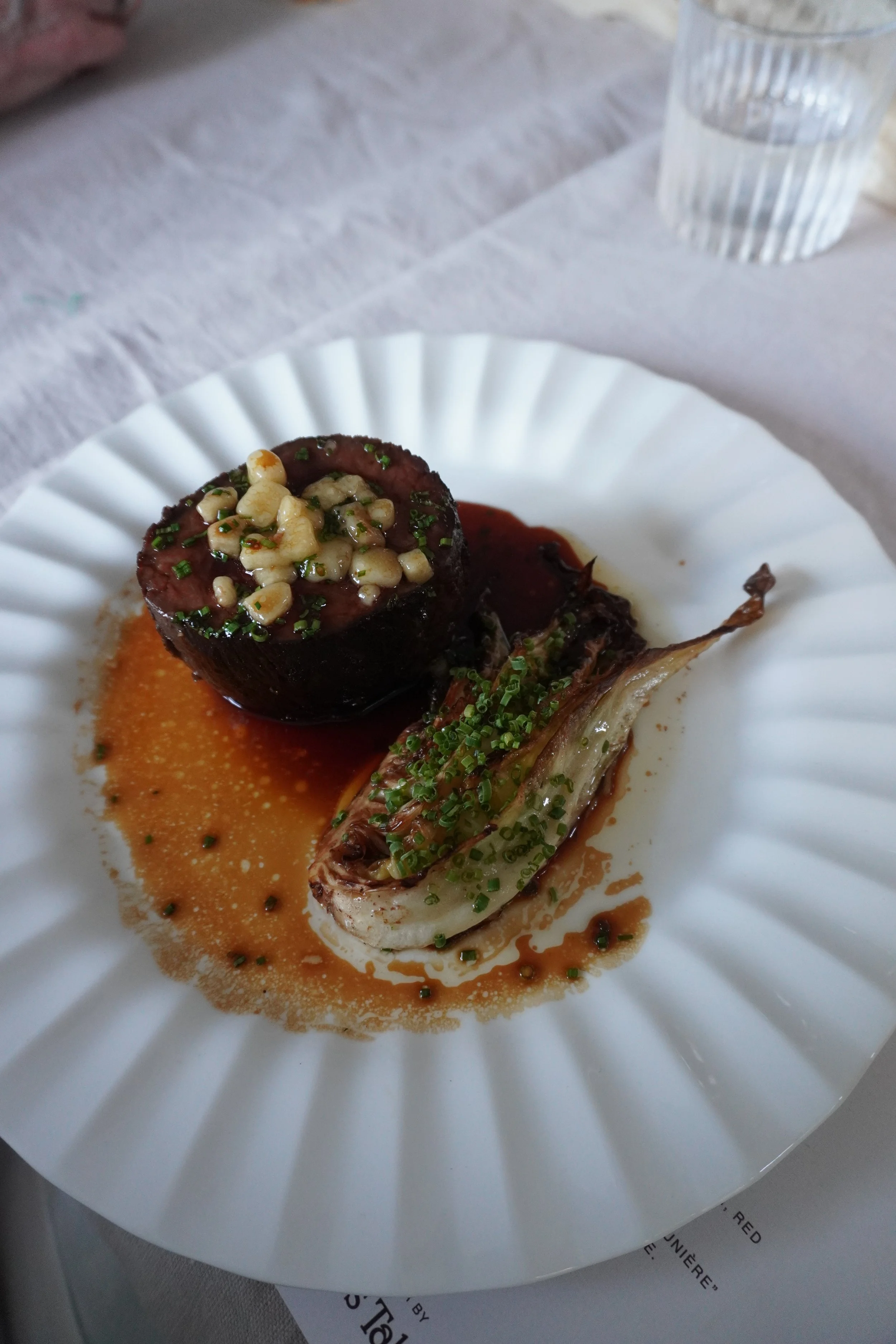 A white plate with meat and garnish at the centre of a dinner table during a private event.
