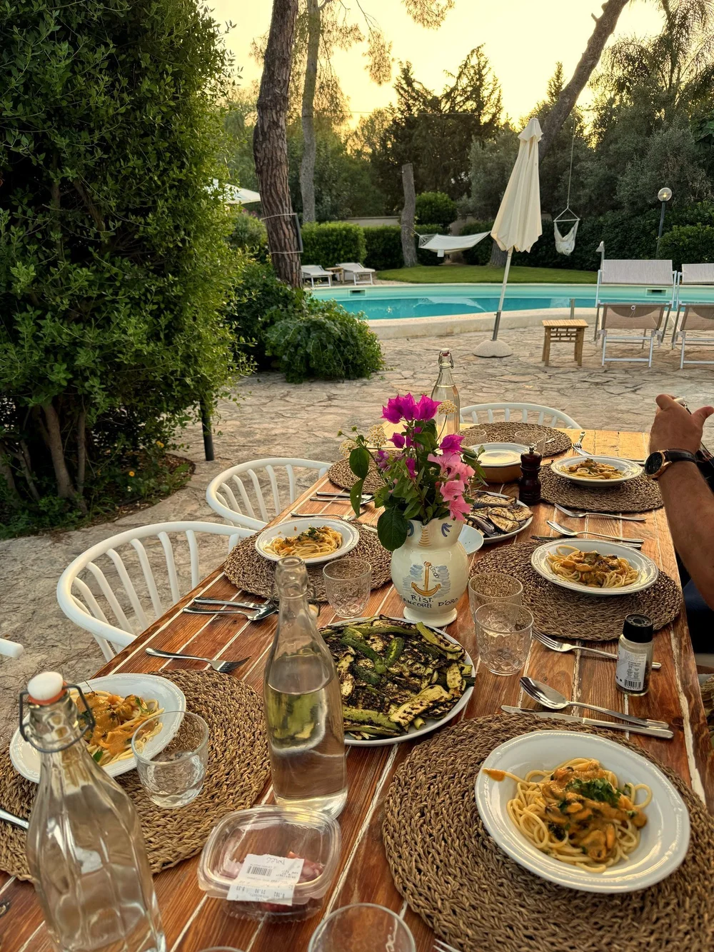 Gedeckter langer Tisch mit Pasta und Gemüse in der Abenddämmerung am Pool