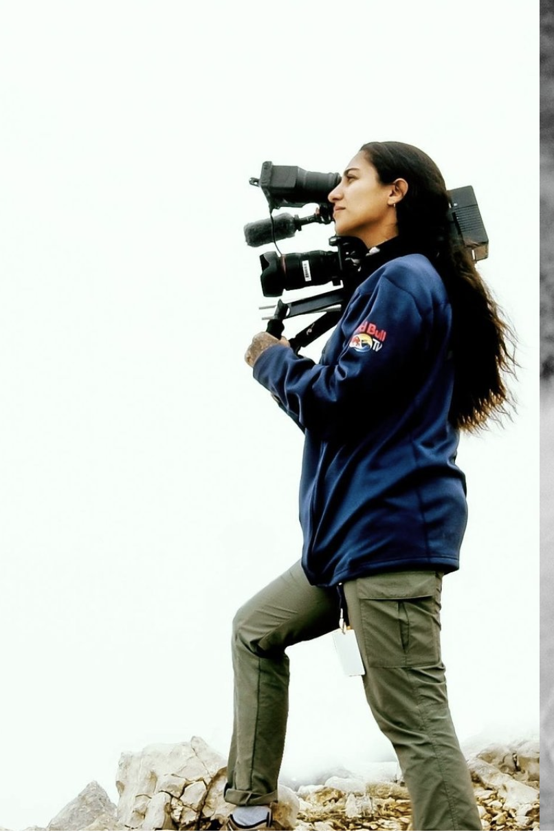 Photographer with a professional video camera on a tripod standing on rocky terrain.