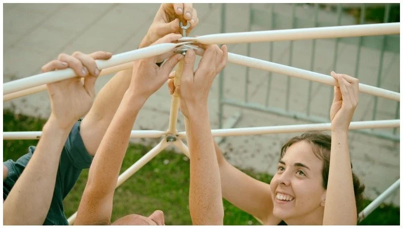 Three people assembling or adjusting a white outdoor drying rack or structure.