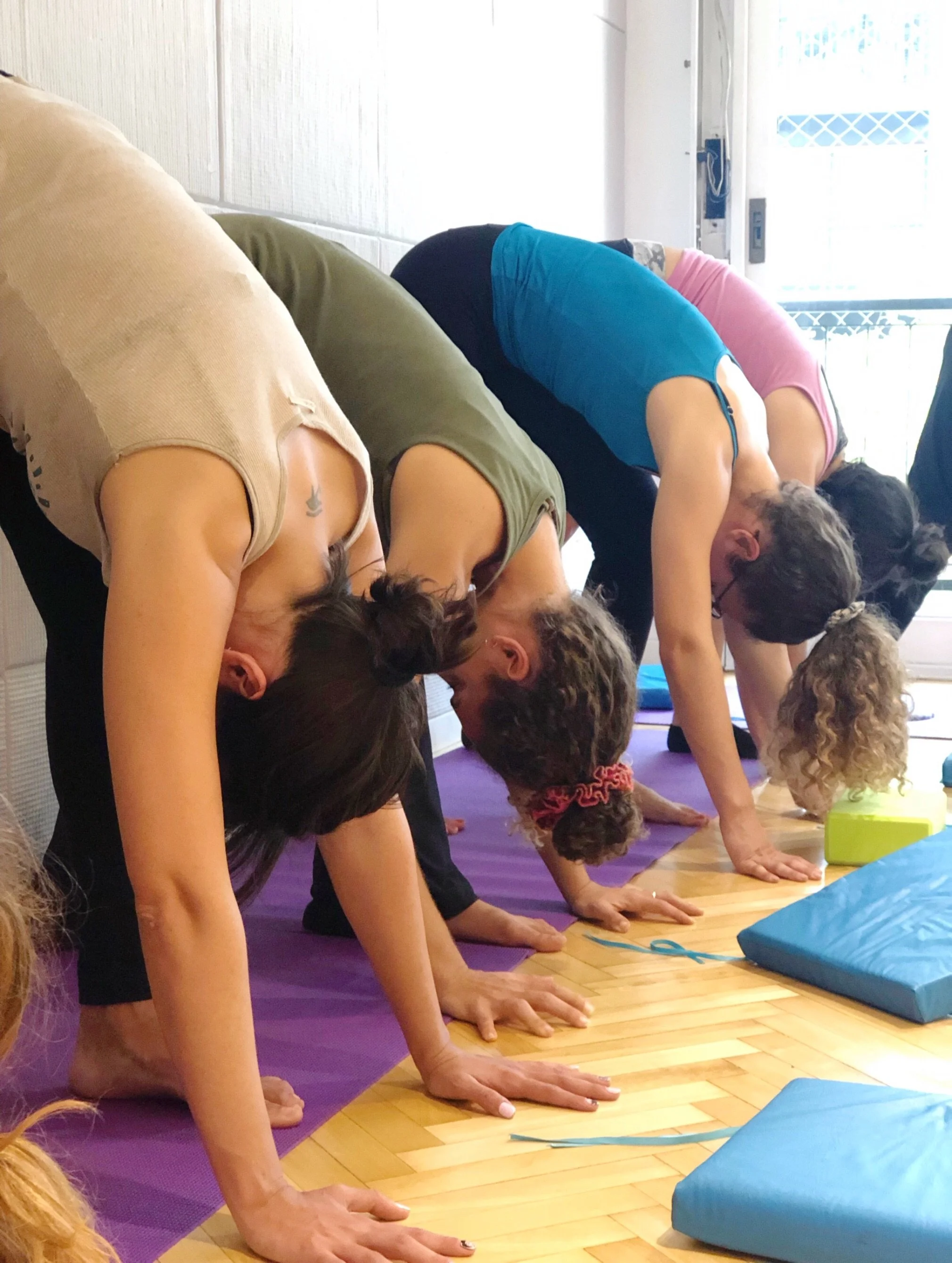 Group of people doing yoga in a studio, bending forward on purple mats.