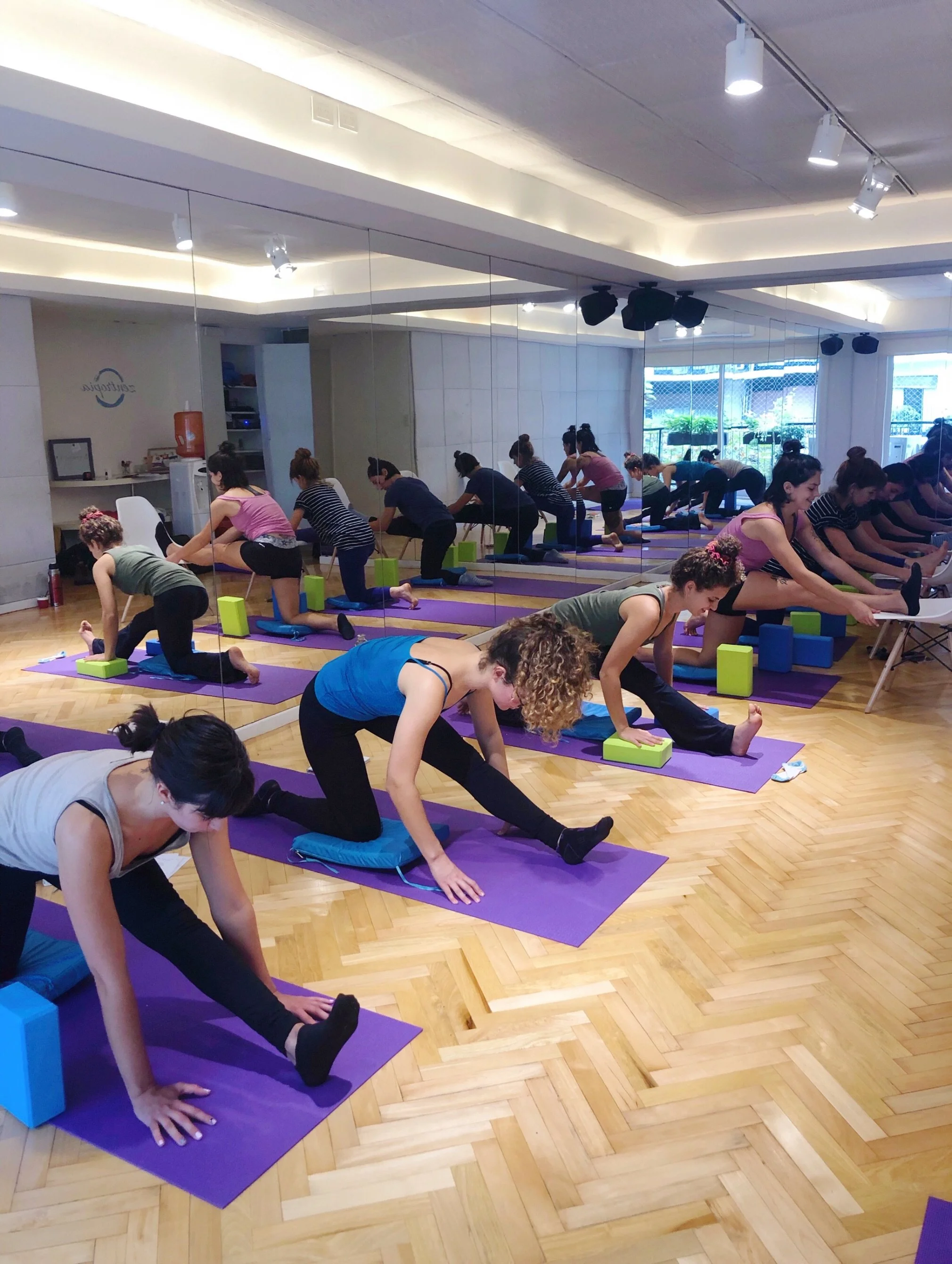 Group of women practicing yoga on purple mats in a fitness studio with mirrors and wood flooring.