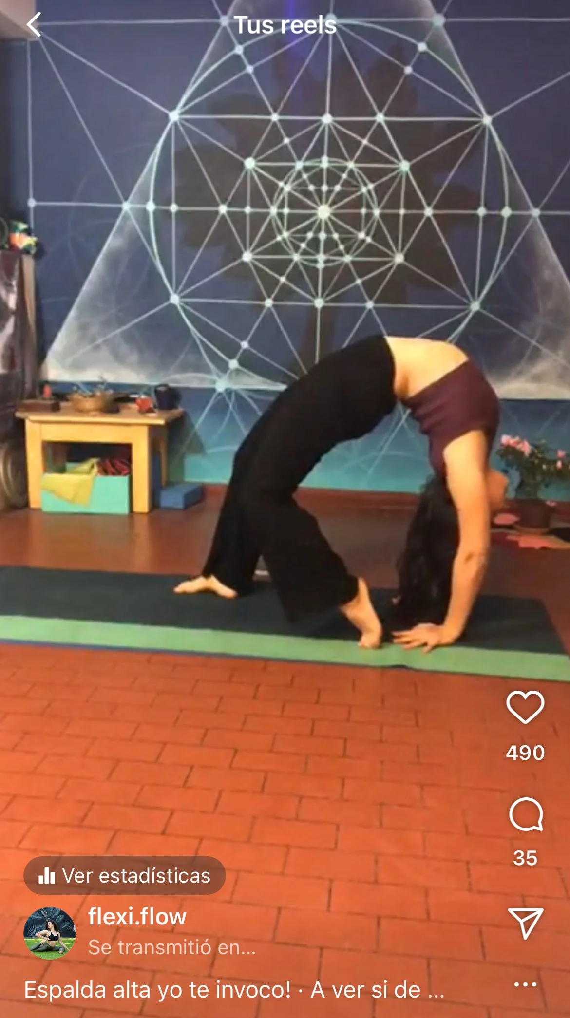 A woman performing a full bridge or wheel in a studio with a geometric wall art design. She is doing a backbend pose on a yoga mat.