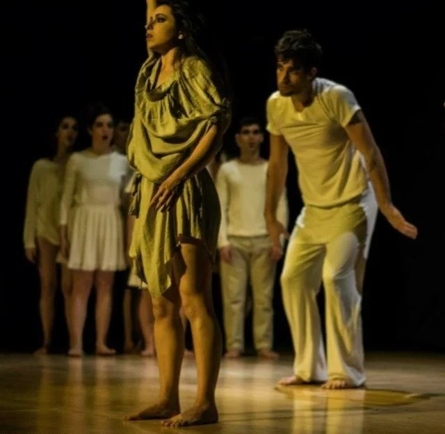 Dancer in gold dress performing with group of dancers in white on stage
