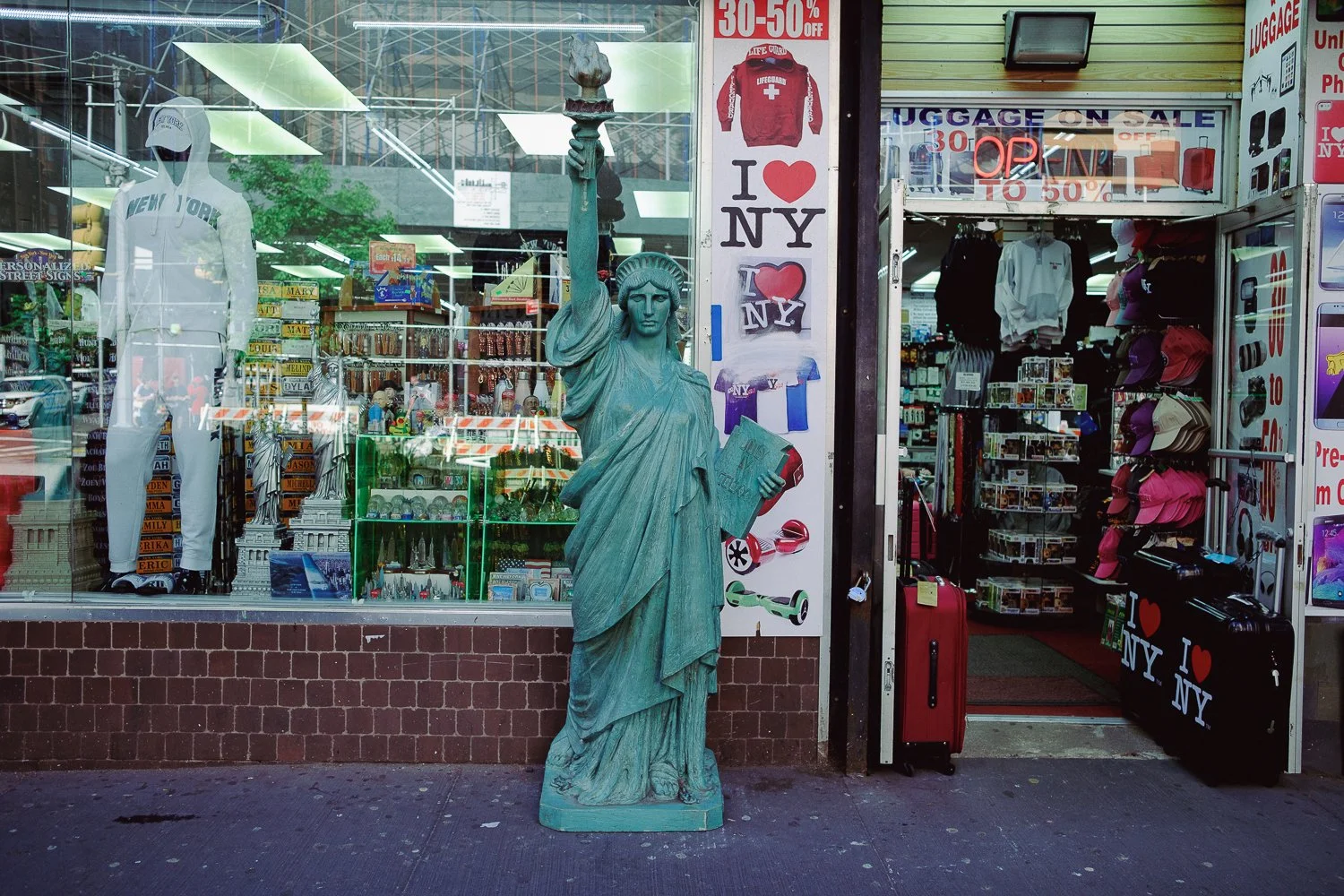 A storefront with 'I love NY' signs, various souvenirs, and a display of clothing, with a replica of the Statue of Liberty in front.